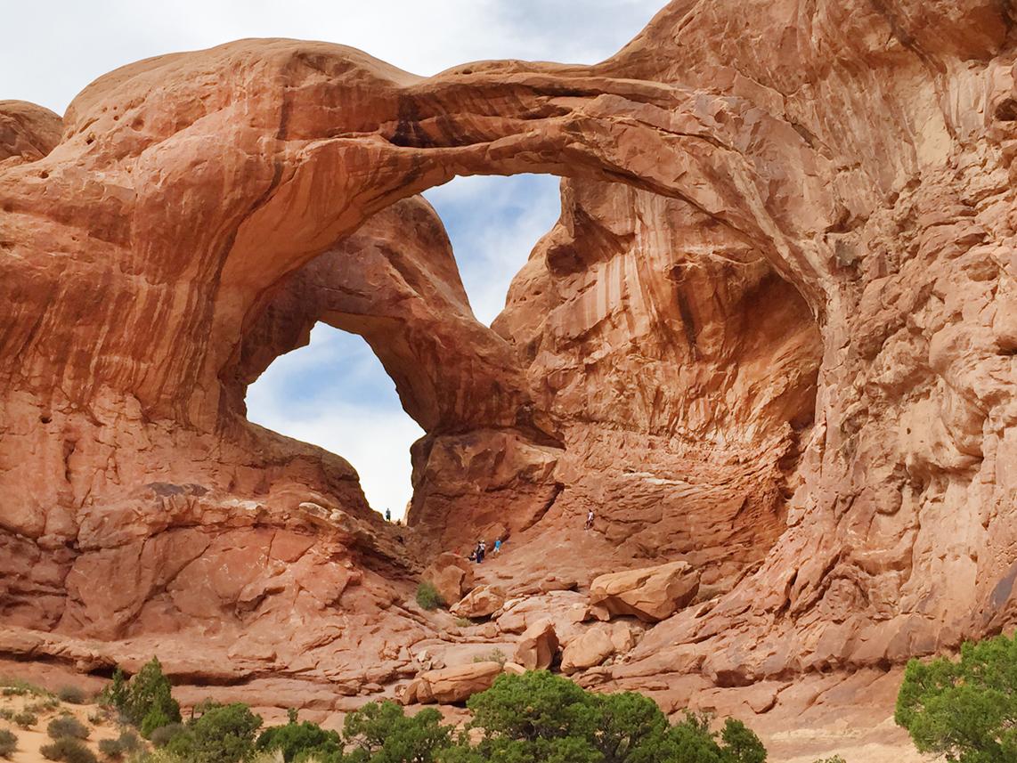 Two large natural arches in red rock, with people walking below.