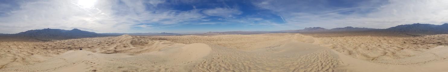 Panoramic view of vast, rippled sand dunes stretching towards distant mountains.
