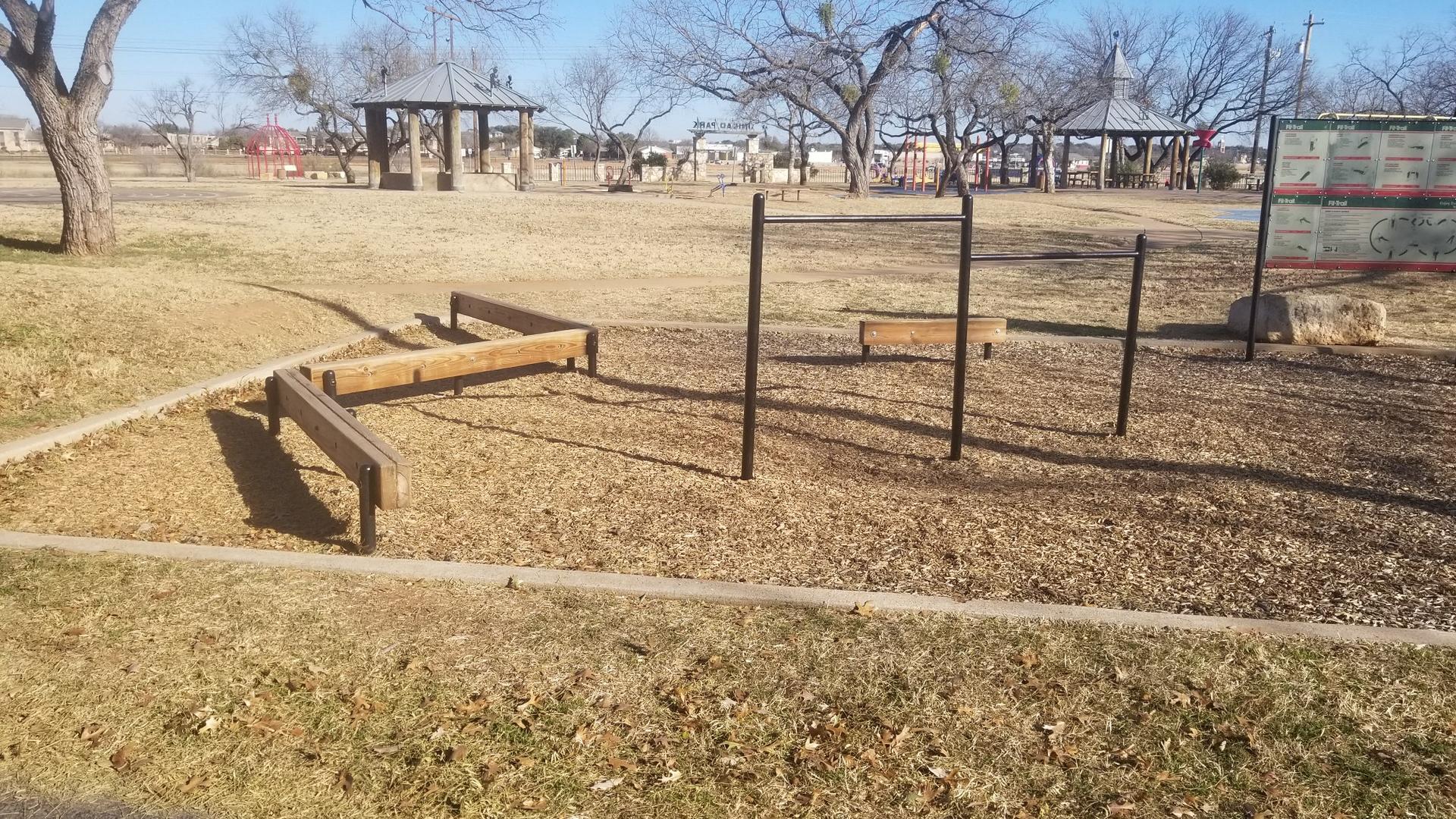 Outdoor fitness equipment on a sunny day in a park with bare trees.