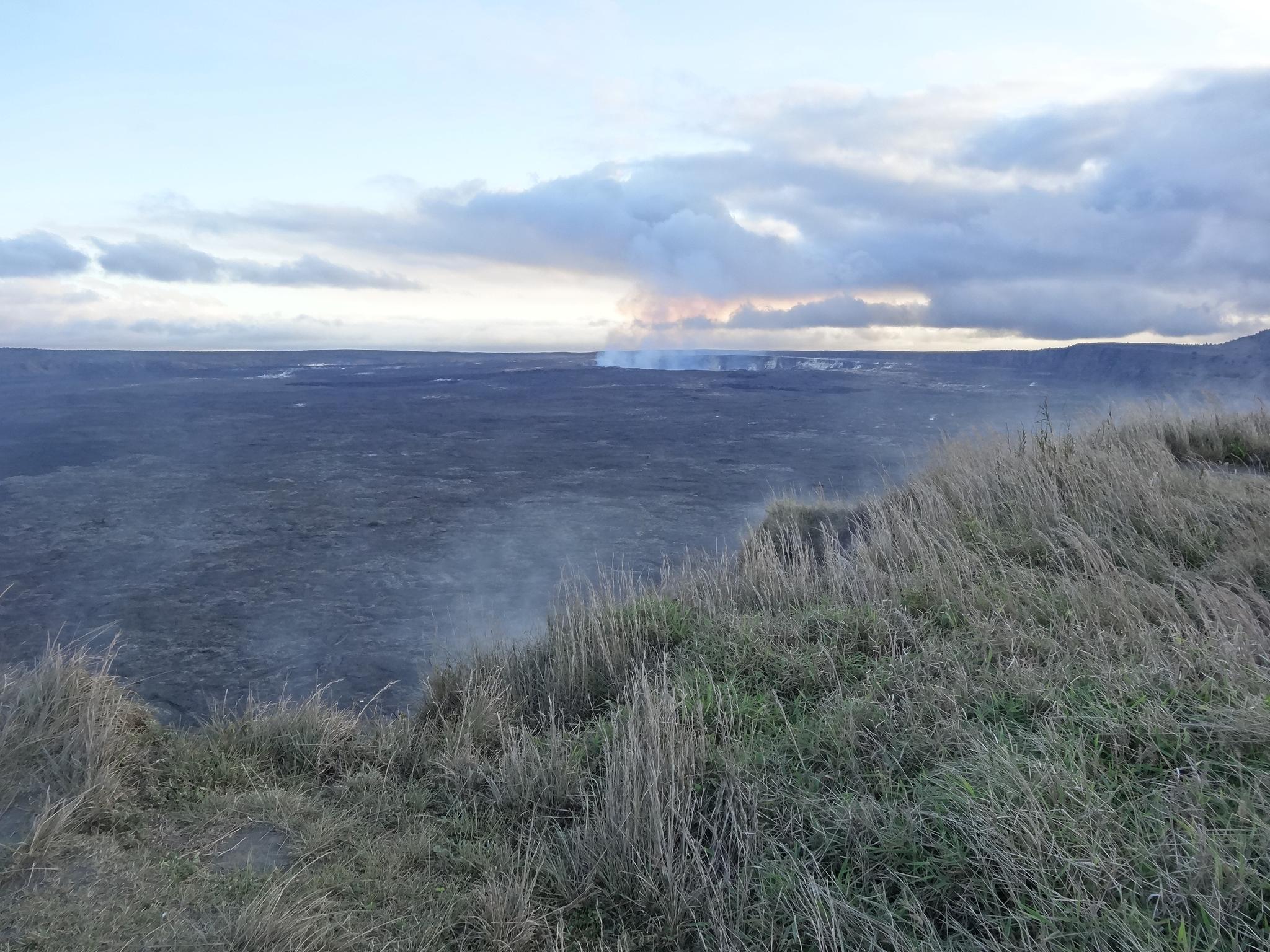 Vast, dark volcanic plain with distant steam plumes under a cloudy sky.