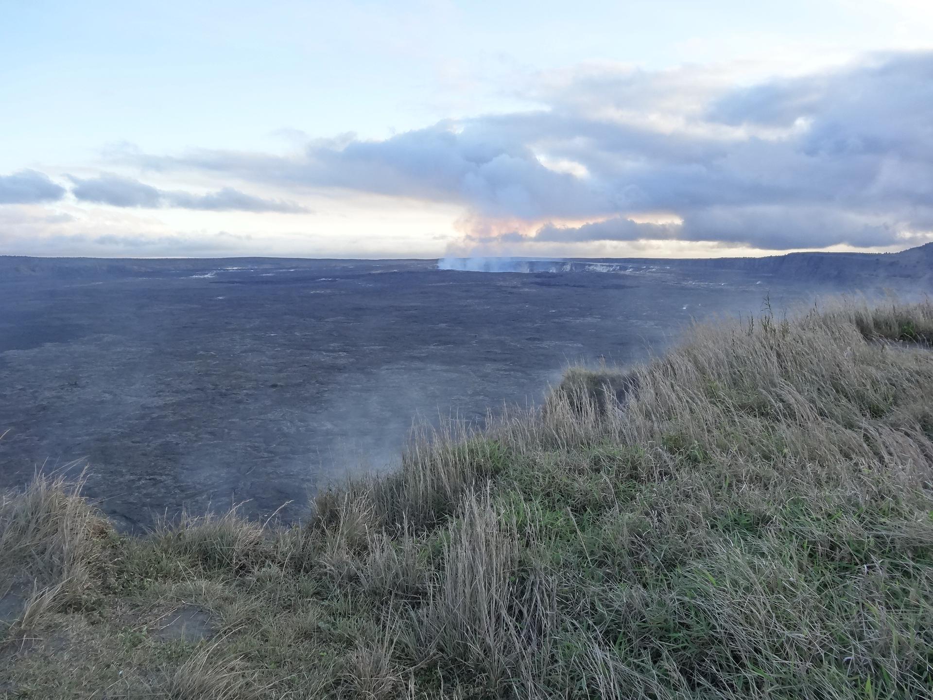 Vast, dark volcanic plain with distant steam plumes under a cloudy sky.