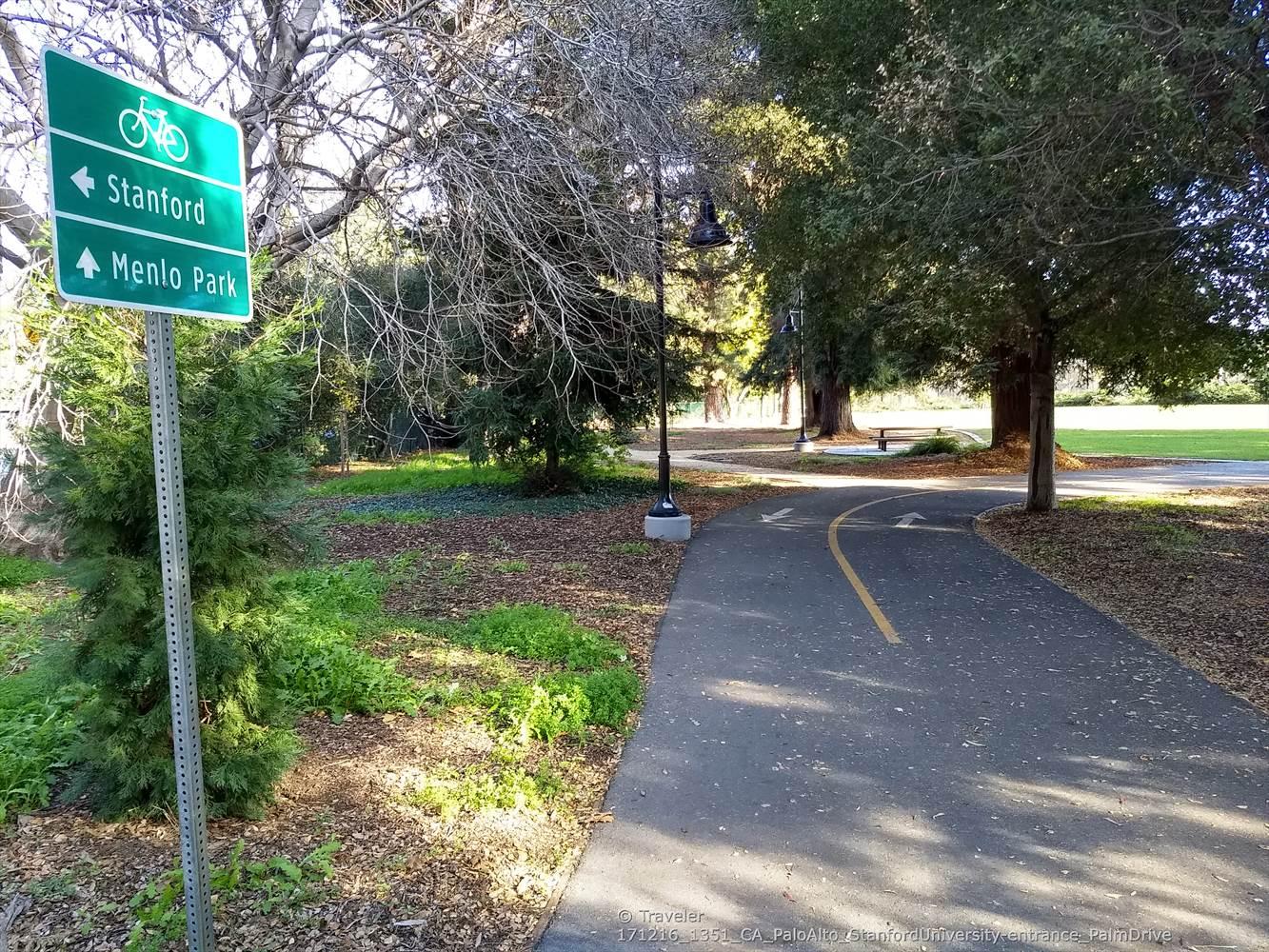 Paved bicycle path with a green sign under bright sunlight.