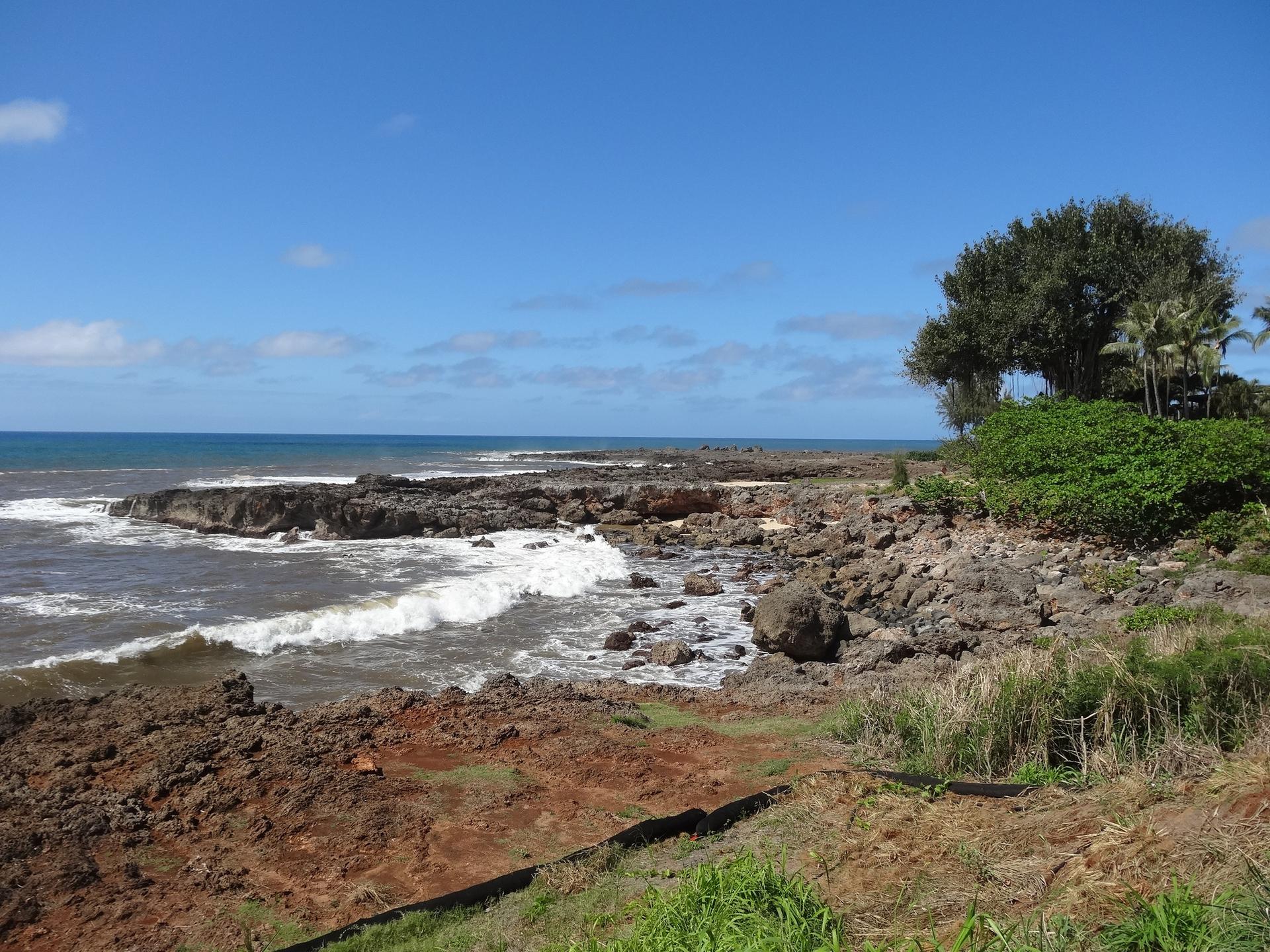 Rugged rocky coastline with waves crashing, under a bright blue sky.