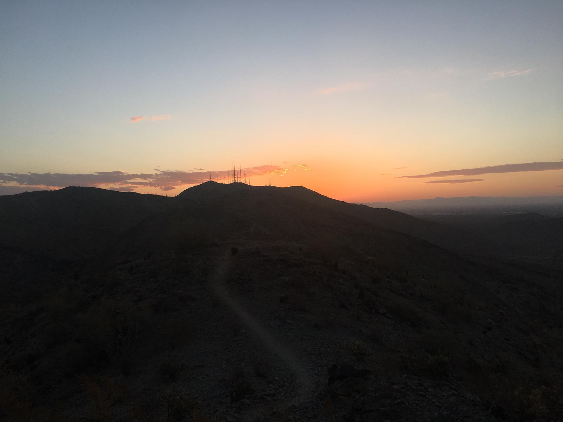 Dark mountain silhouette at sunset with winding path and distant towers.