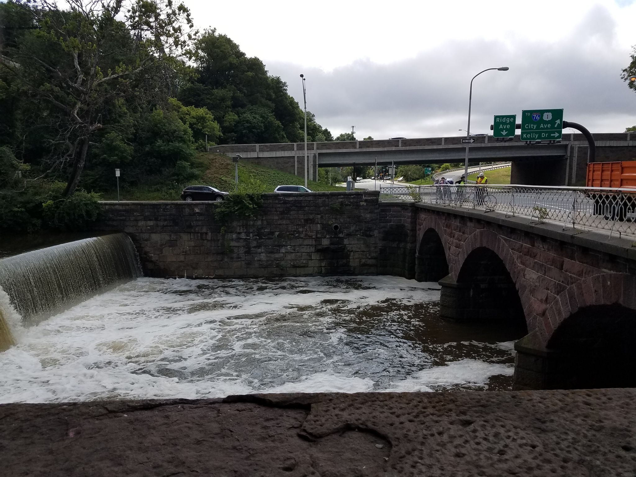 Stone bridge over dam with rushing water, highway overpass, overcast day. - Wissahickon Creek Waterfall – Kitchen's Lane bridge loop from Wissahickon