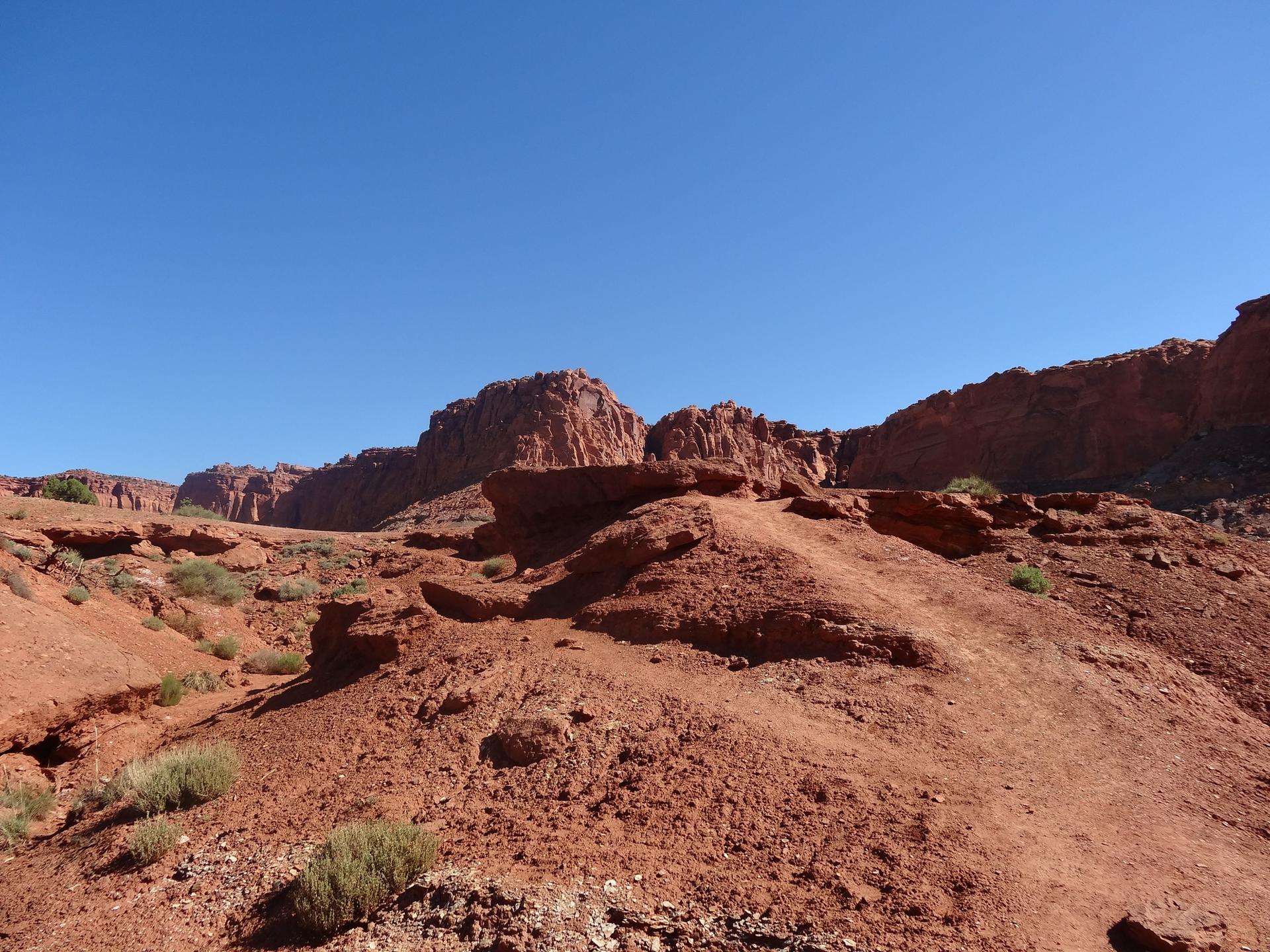 Sunny desert landscape with red rock formations under a clear blue sky.