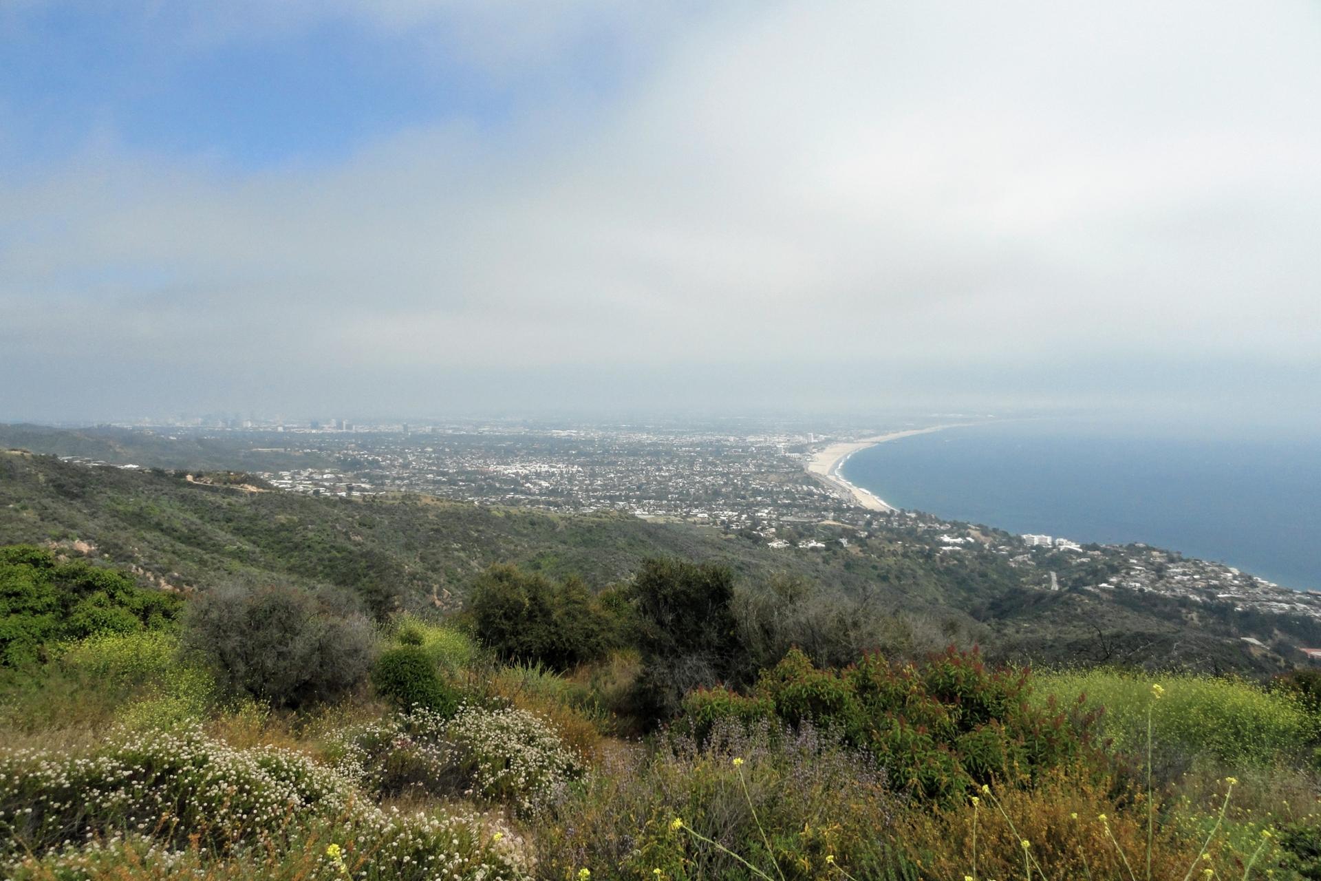 A wide view of a coastal city, beach, and ocean under a cloudy sky.