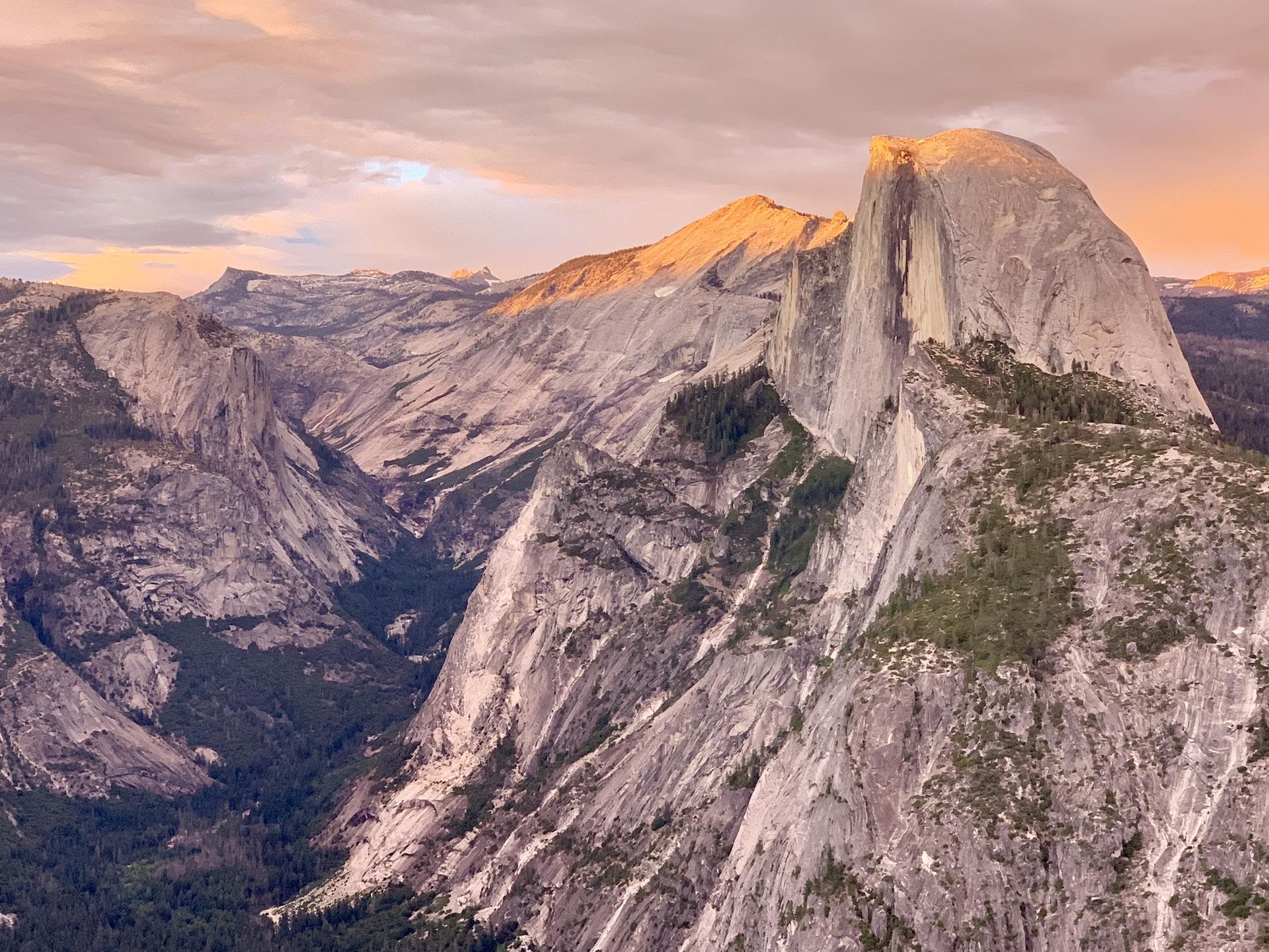 Majestic granite mountains bathed in warm golden hour light under a cloudy sky.