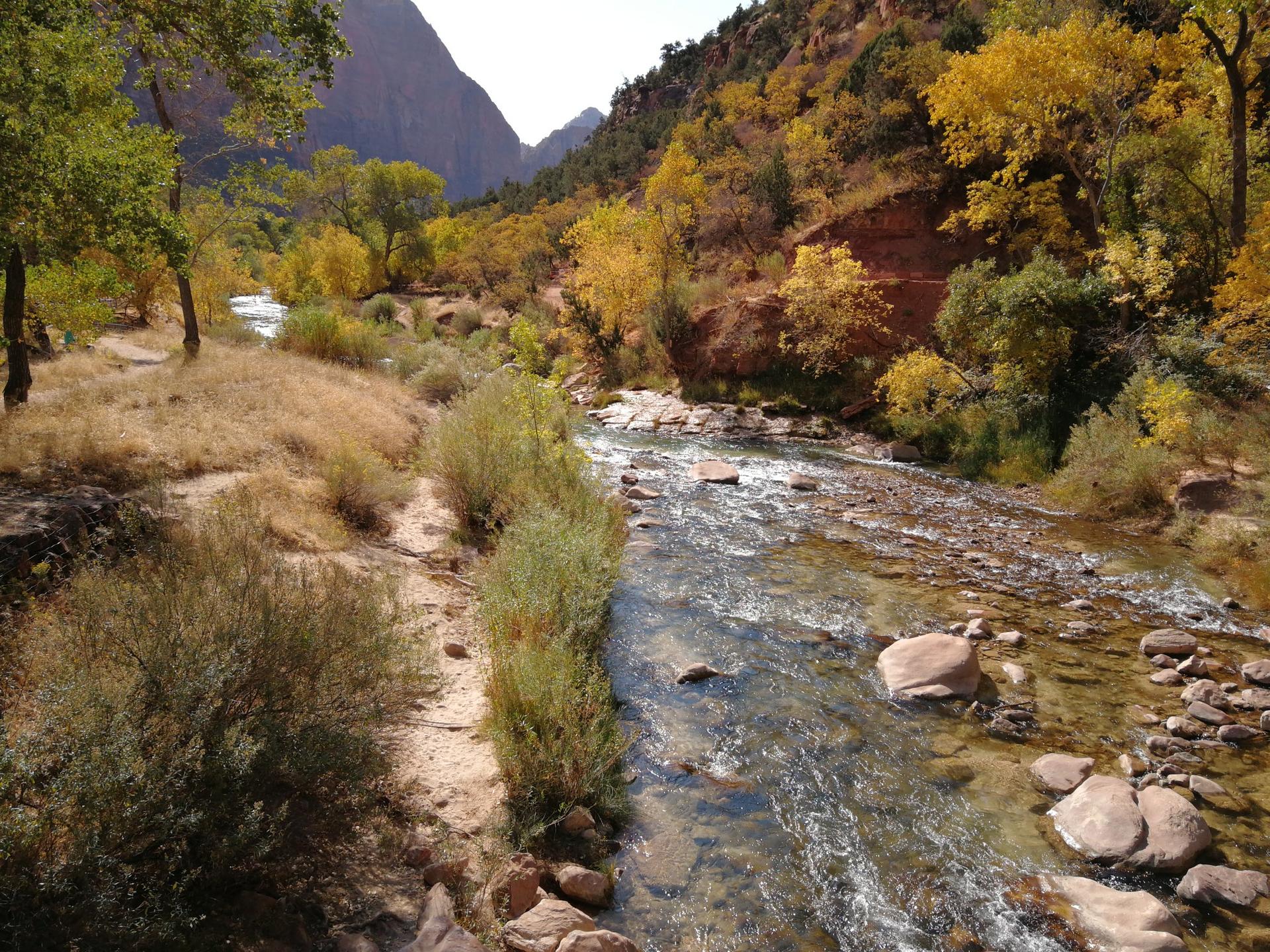 A river flows through a valley with autumn-colored trees and rocky banks.
