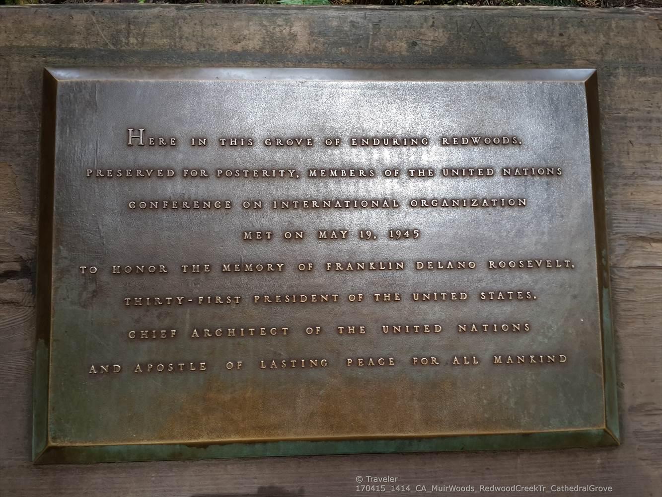 A bronze plaque with engraved text, mounted on a wooden surface.