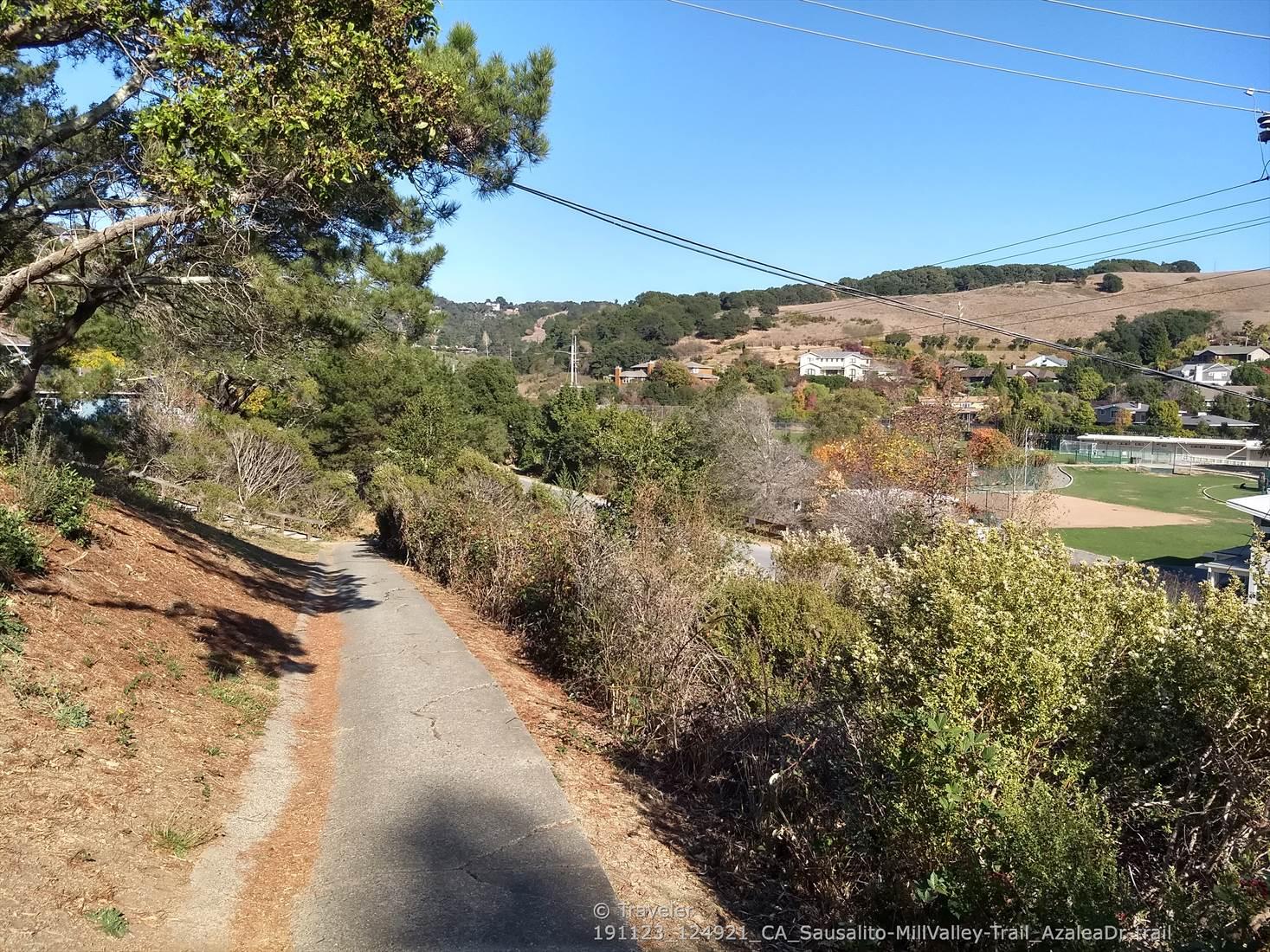 Paved path alongside a grassy slope, leading to a distant field.