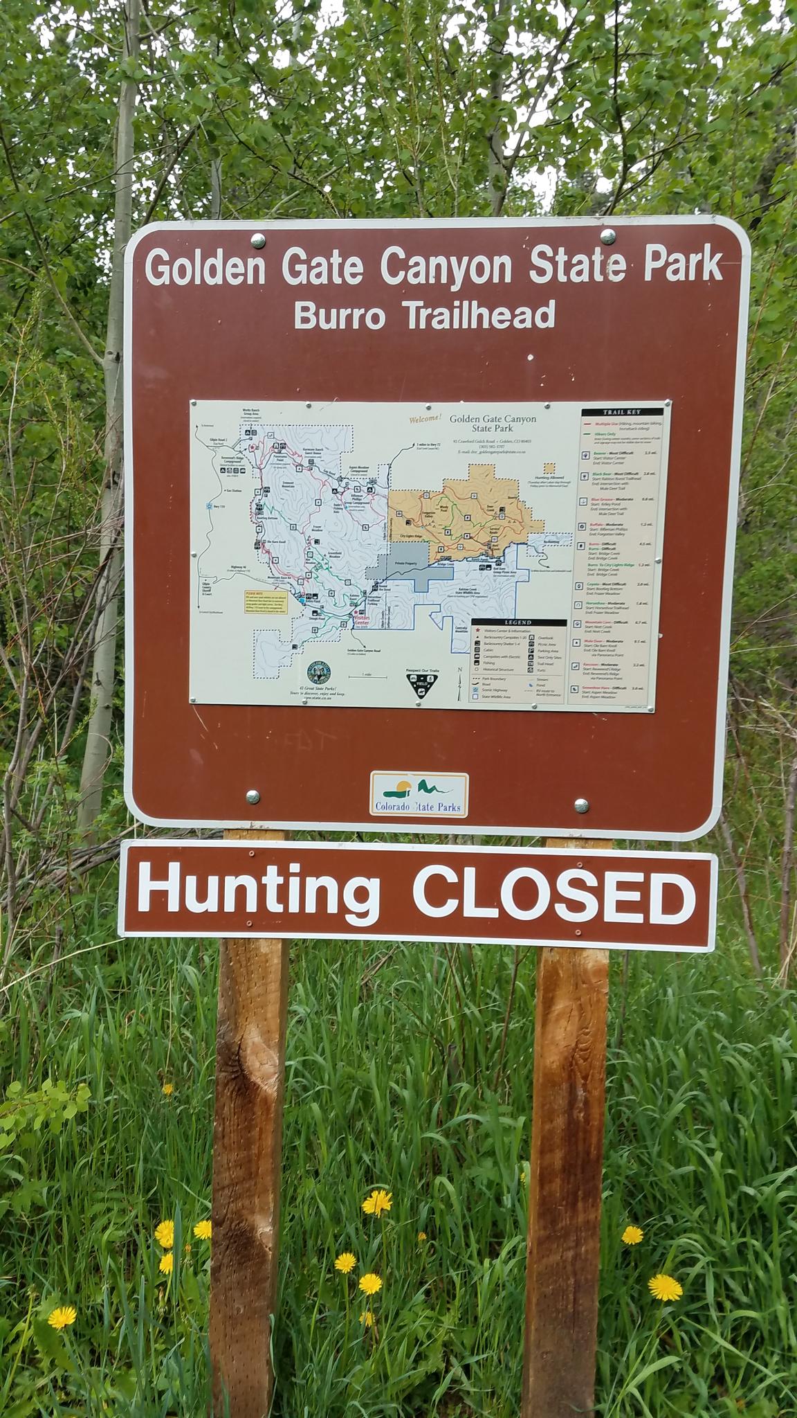 A brown park sign with a map and "Hunting Closed" stands in green foliage.