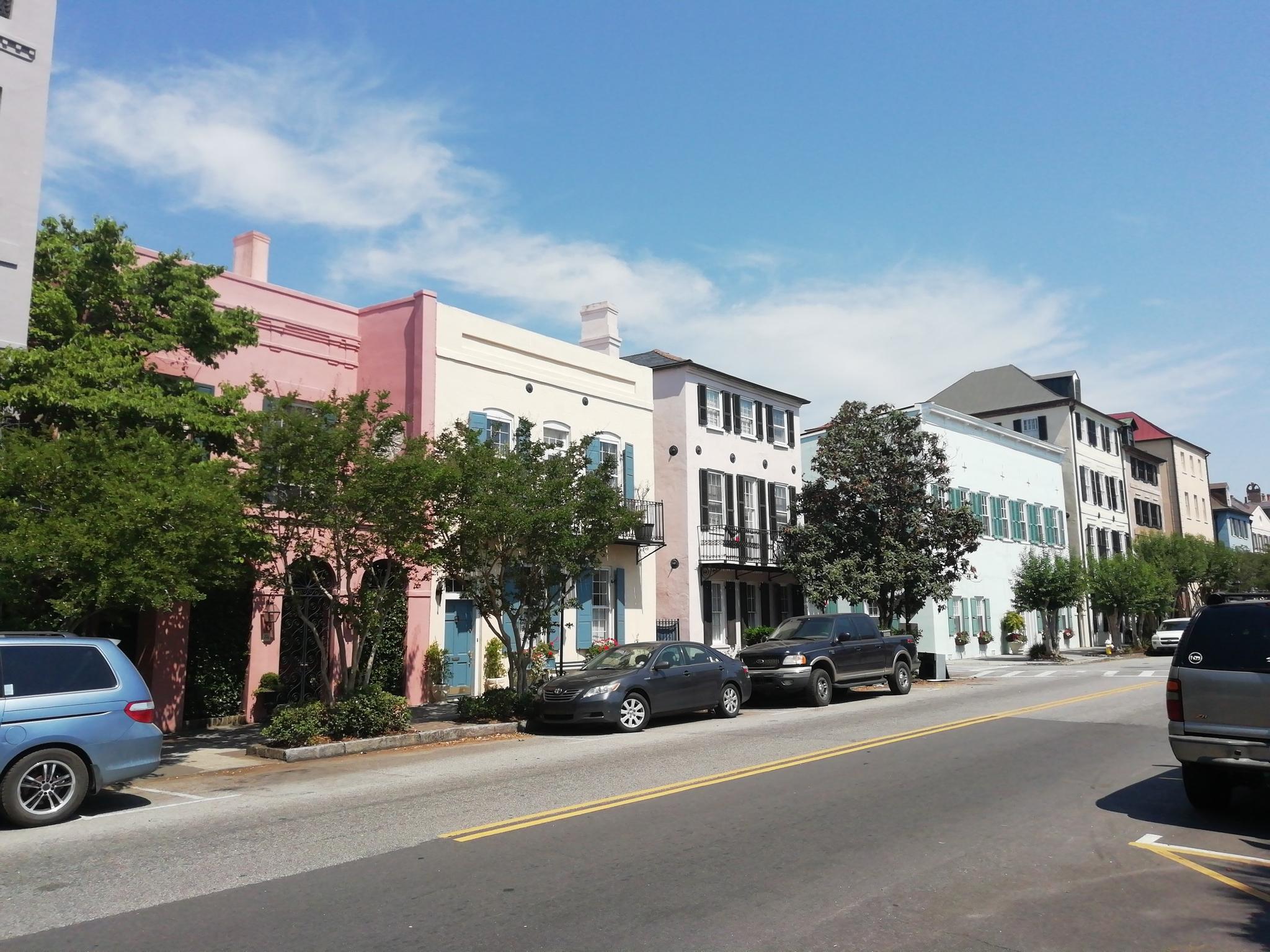 Colorful historic buildings line a sunny street with parked cars and green trees.
