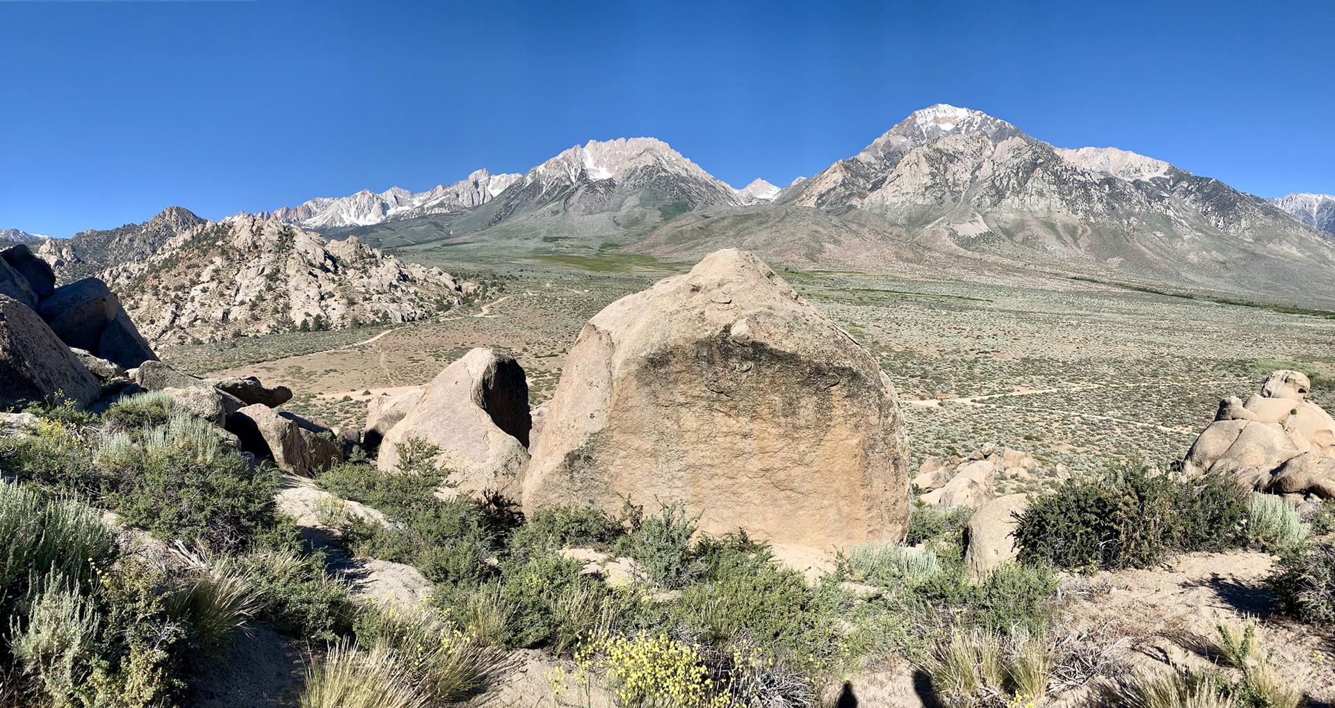 Large boulders in arid landscape with distant snow-capped mountains under clear sky.