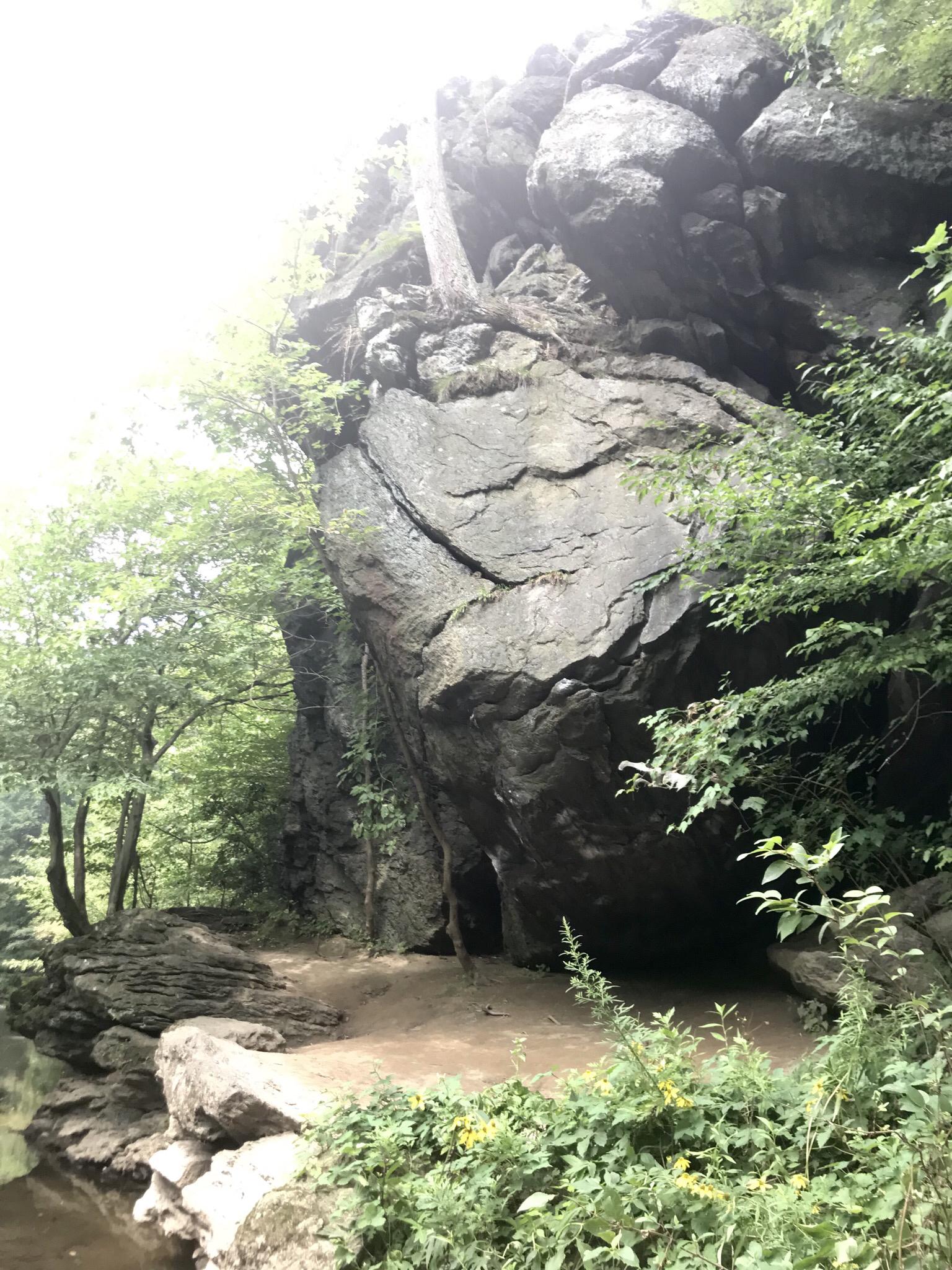 Massive rock formation with a cave-like opening, surrounded by green trees.