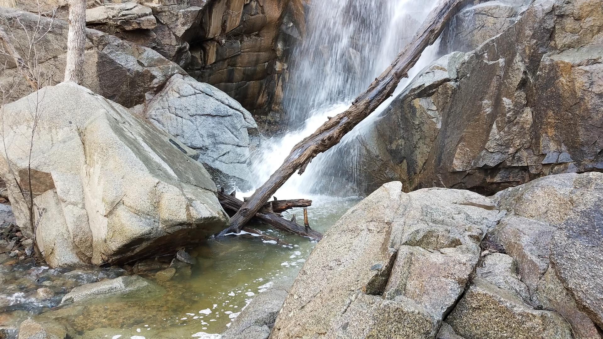 Waterfall cascading over rocks with a fallen log, creating a pool.