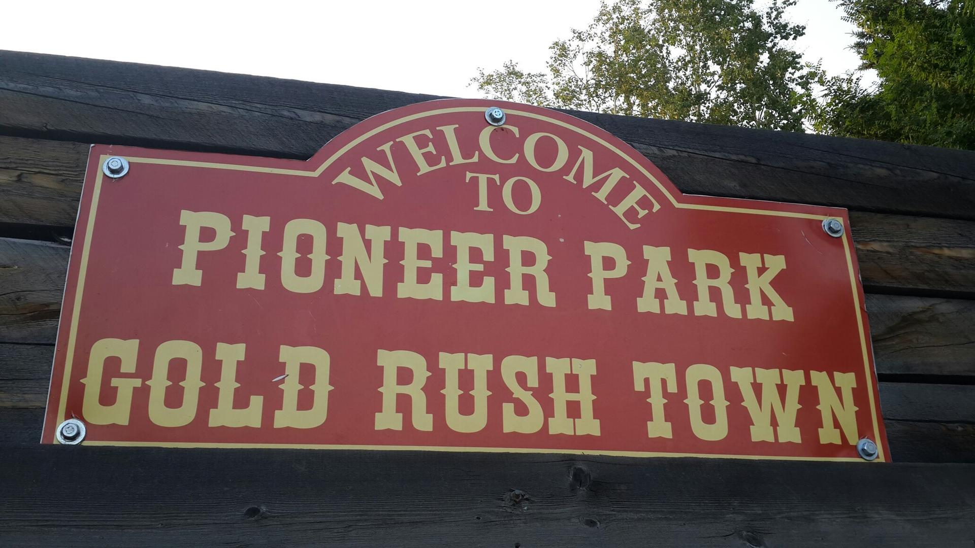 A red sign with yellow text welcoming visitors to a gold rush themed area.