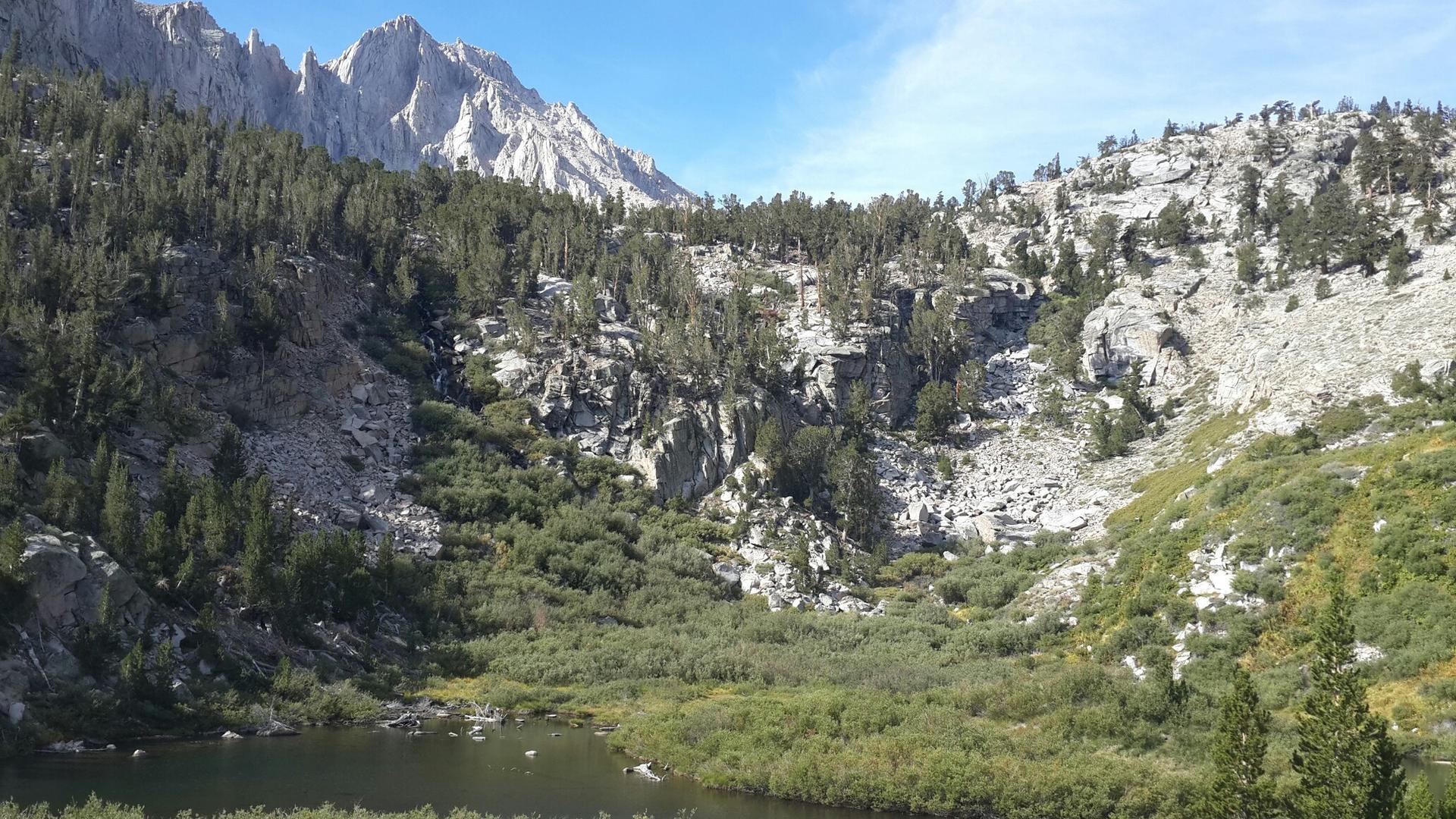 Mountain lake surrounded by rocky slopes and pine trees on a bright day.
