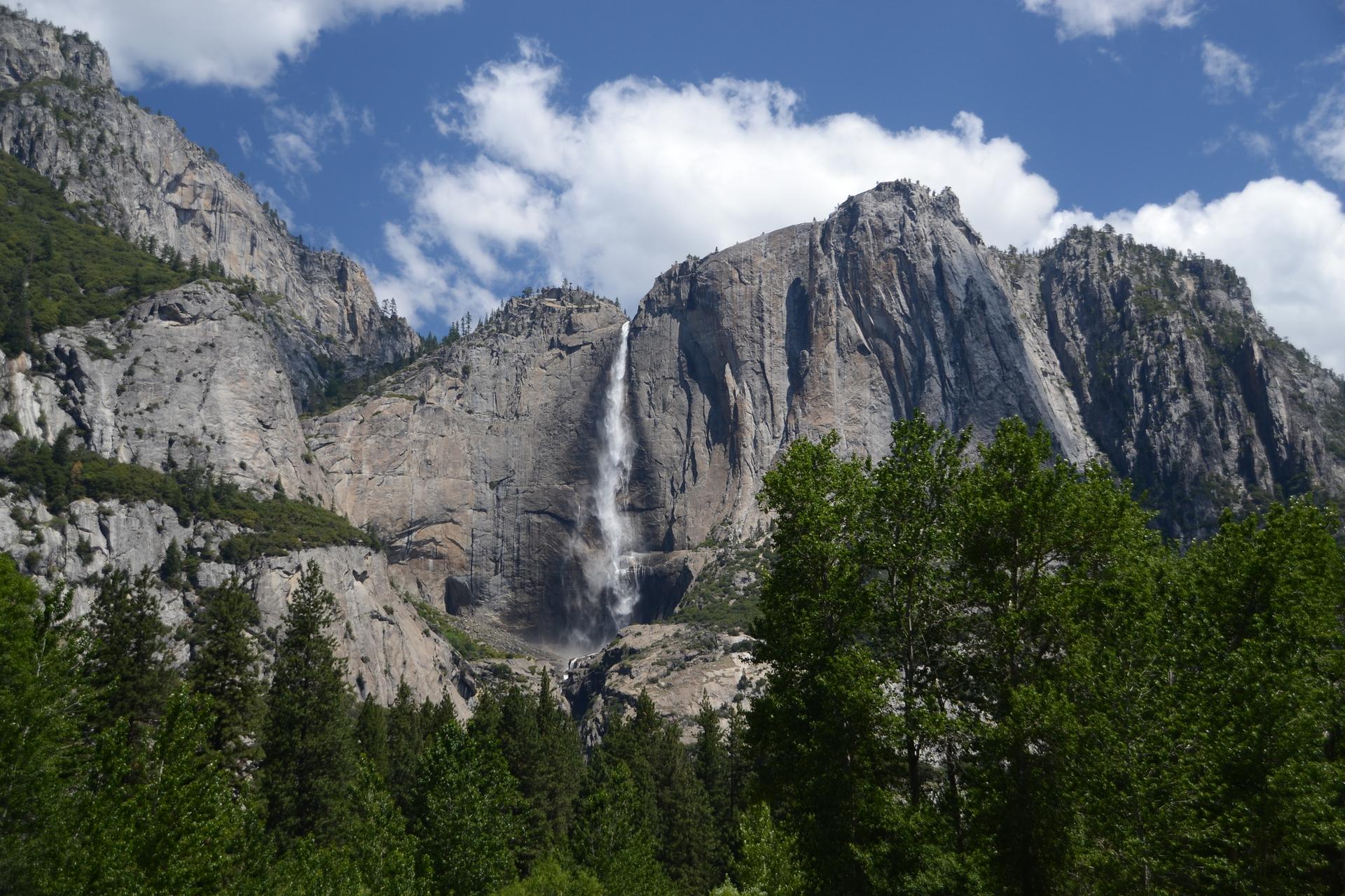 Majestic waterfall plunges down a sheer rock face, surrounded by green trees.