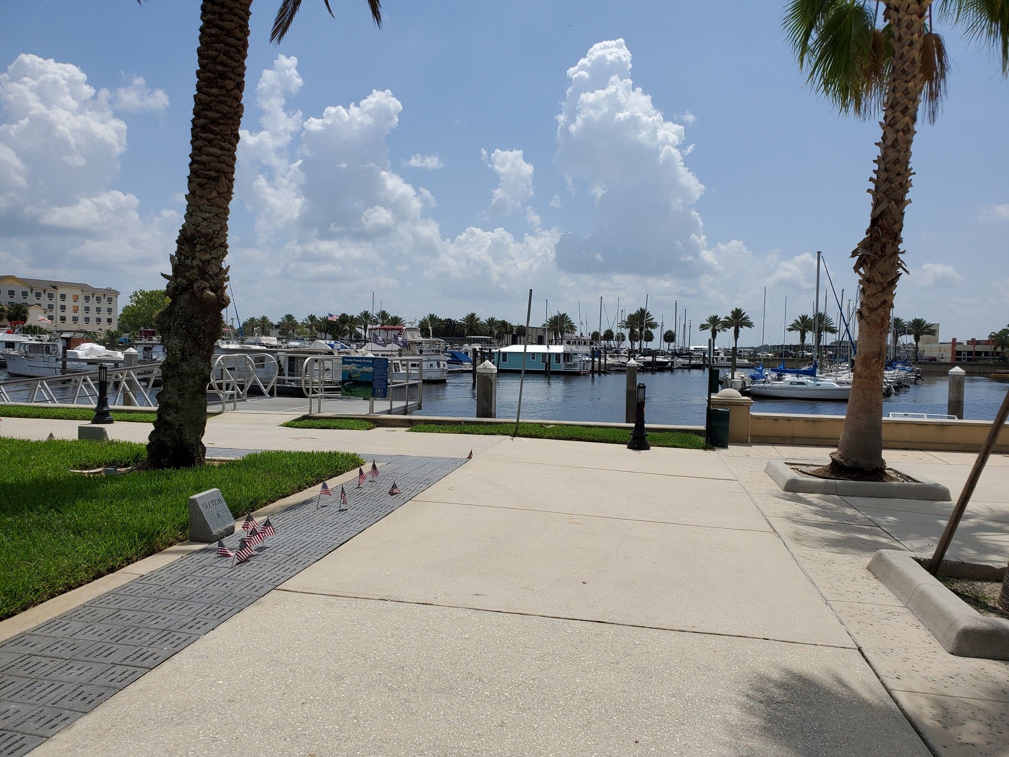 Bright marina scene with boats docked, palm trees, and a paved path. - Veterans Memorial Park Sanford – Monroe Marina loop from Sanford