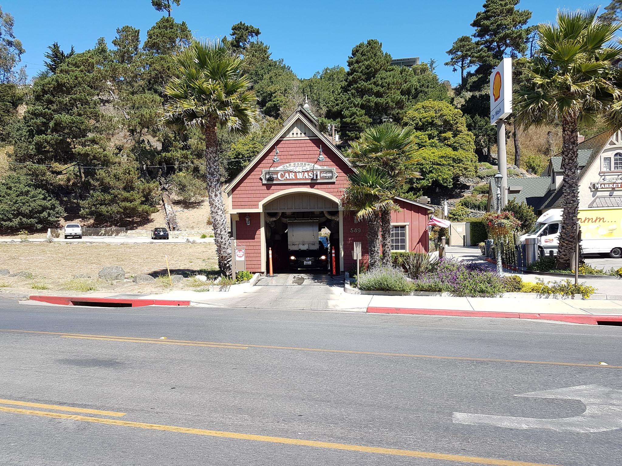 Red car wash building with a car inside, surrounded by palm trees on a sunny day.