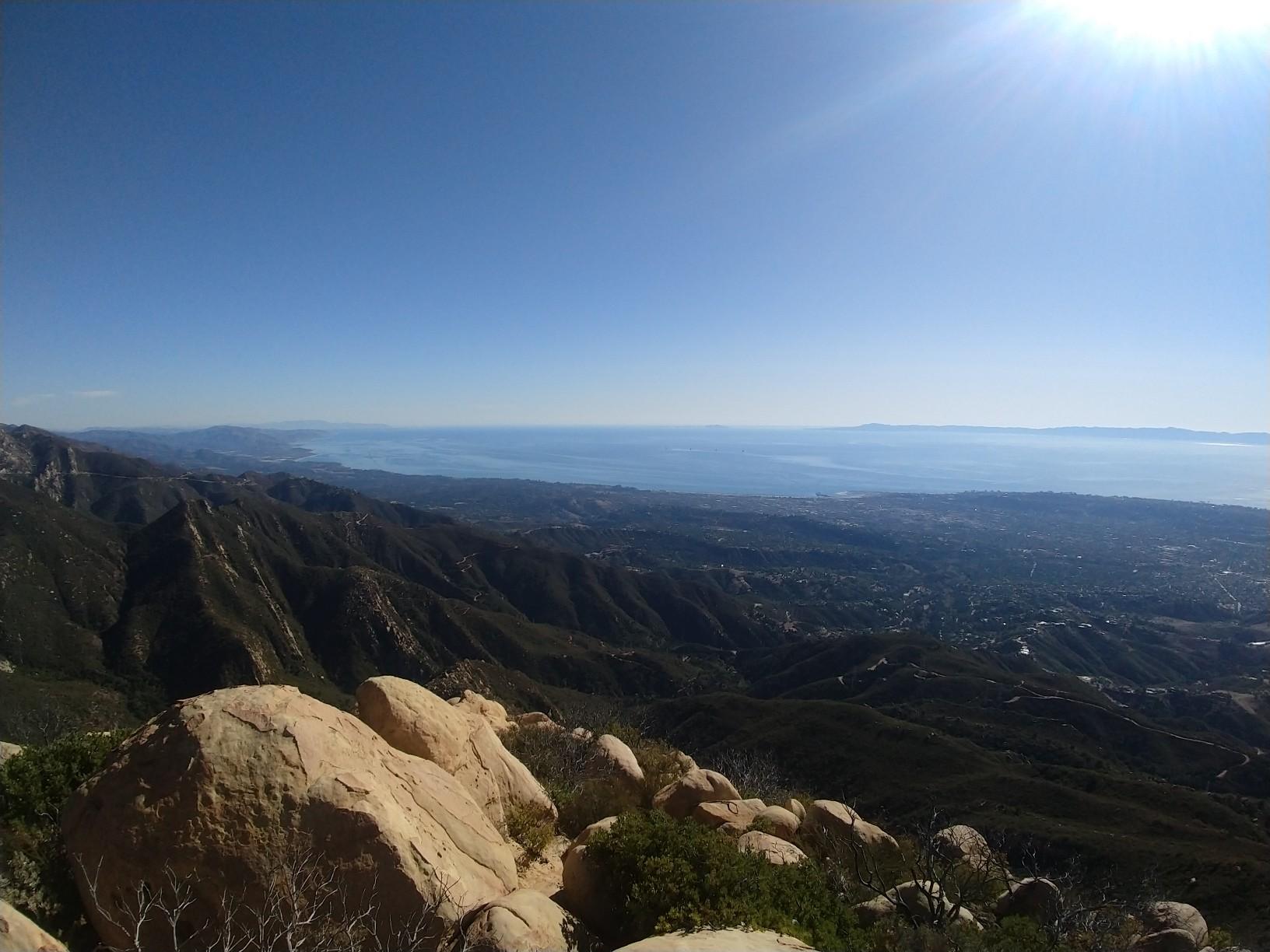 Bright sunny view from rocky mountain peak overlooking ocean and valley.