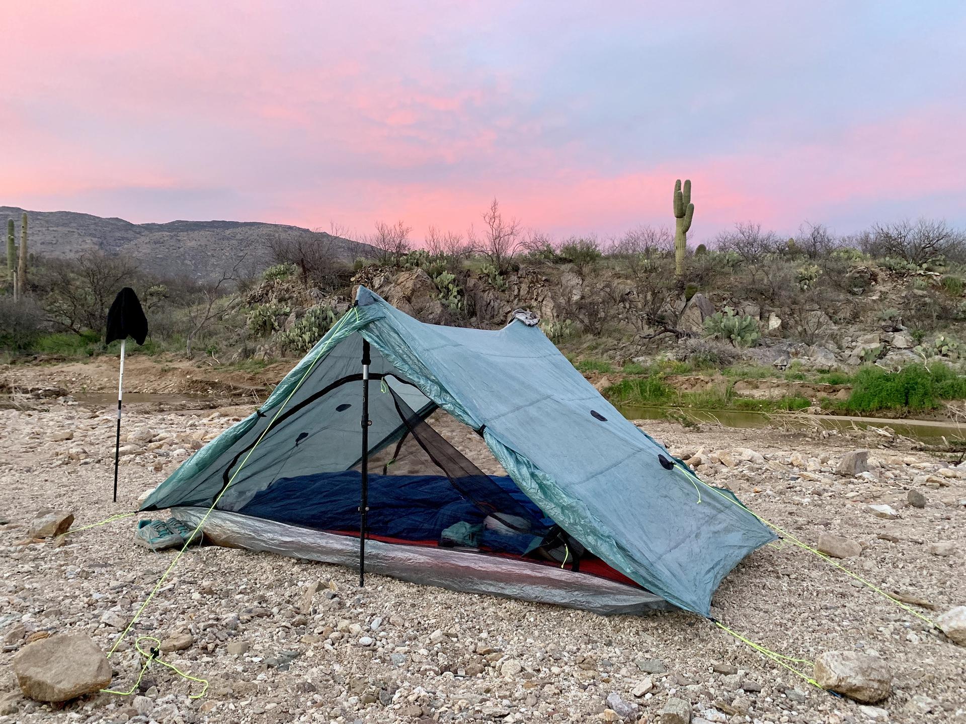 Light blue tent set up on rocky ground under a vibrant pink sunset sky.