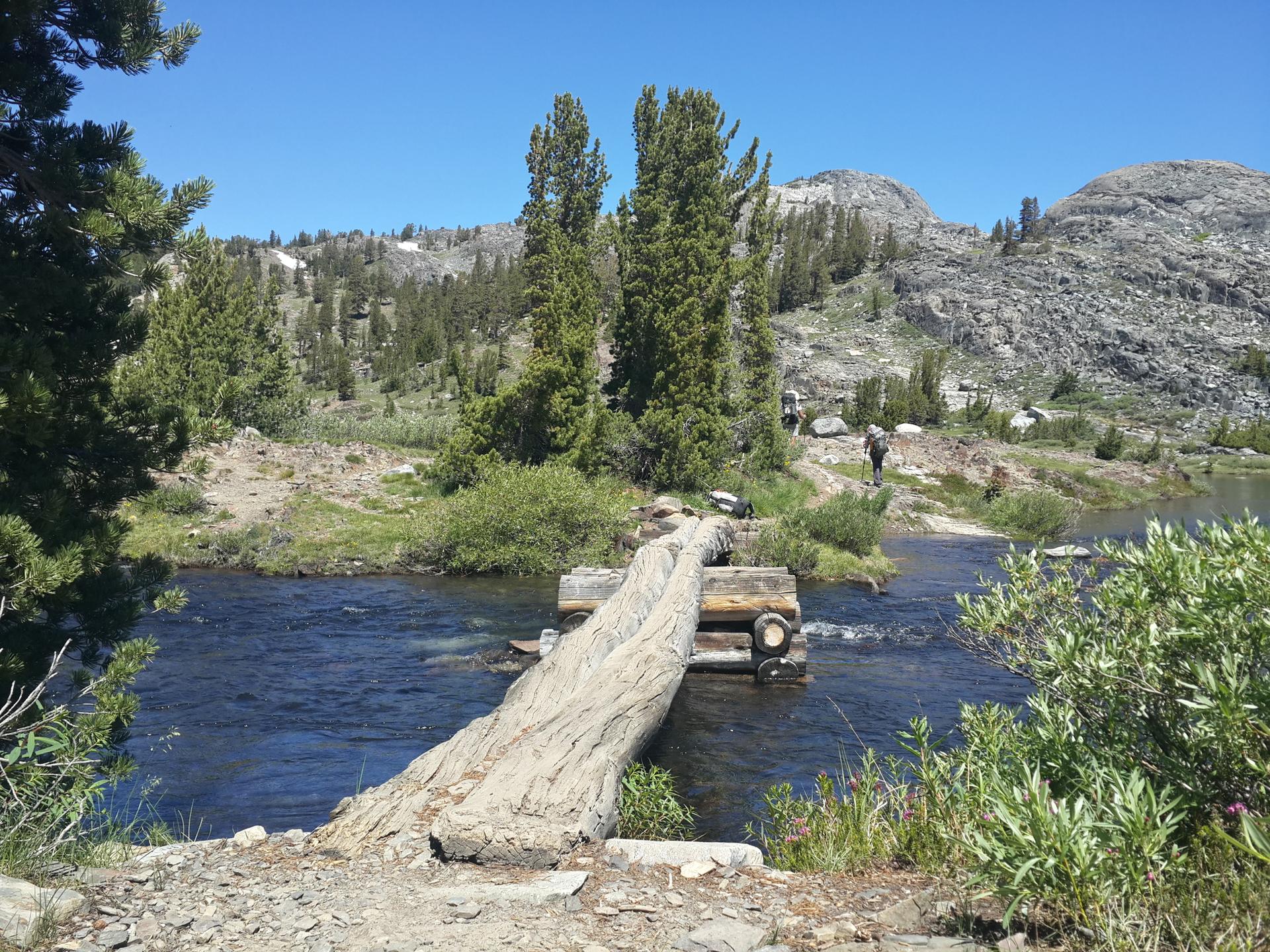 Log bridge over a river flowing into a lake on a sunny day.