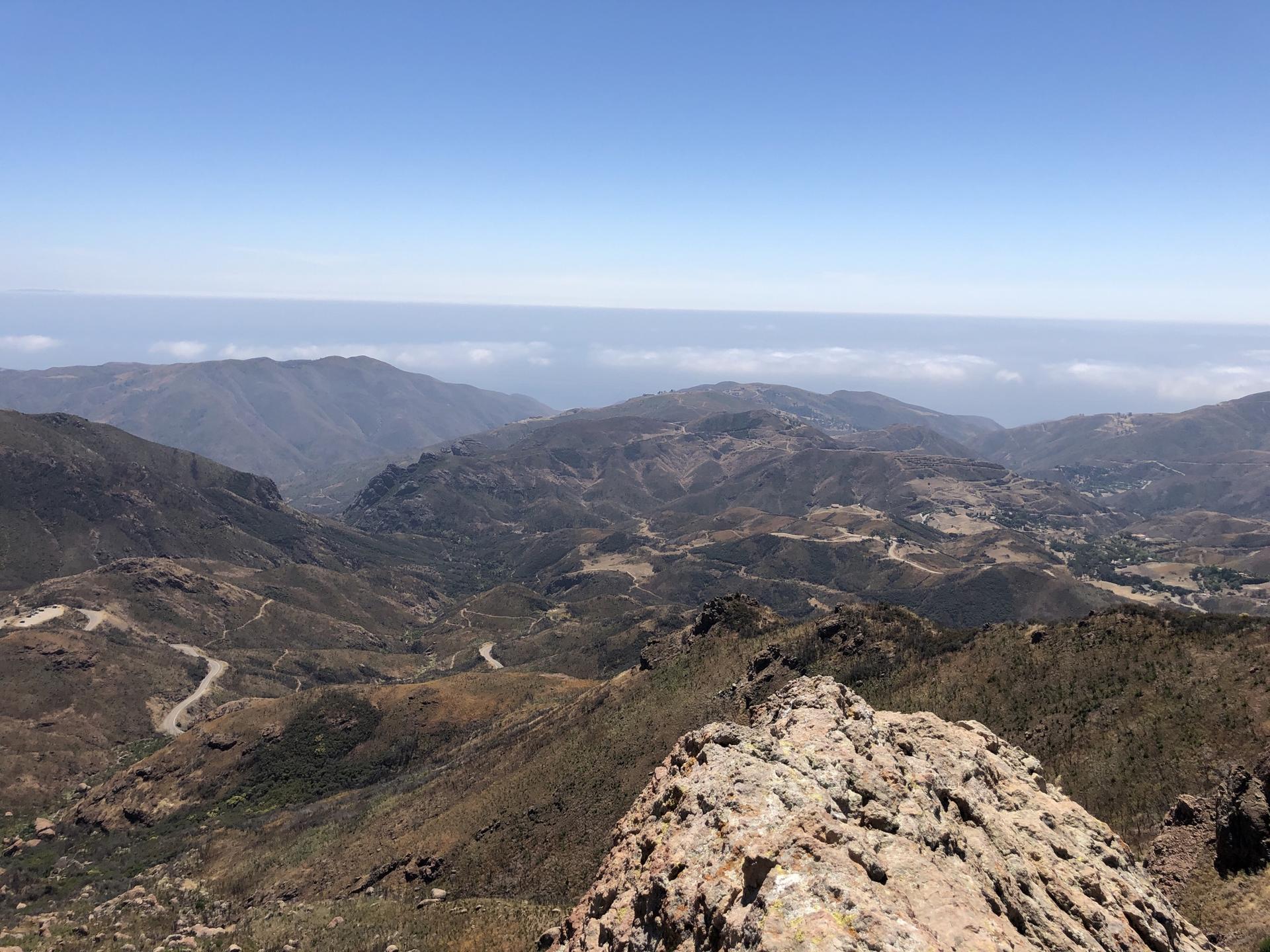 Expansive mountain vista under clear blue sky, with distant hazy ocean.