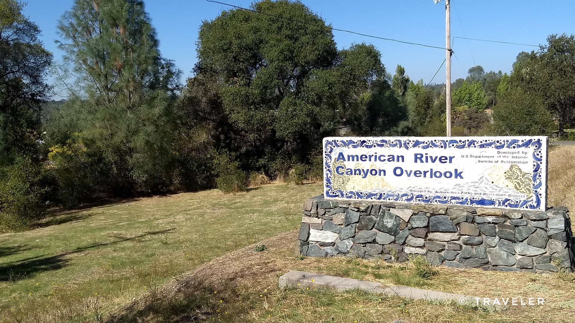 A large, decorative sign on a stone base in a sunny, grassy field. - Robie Point Loop via Western States Trail