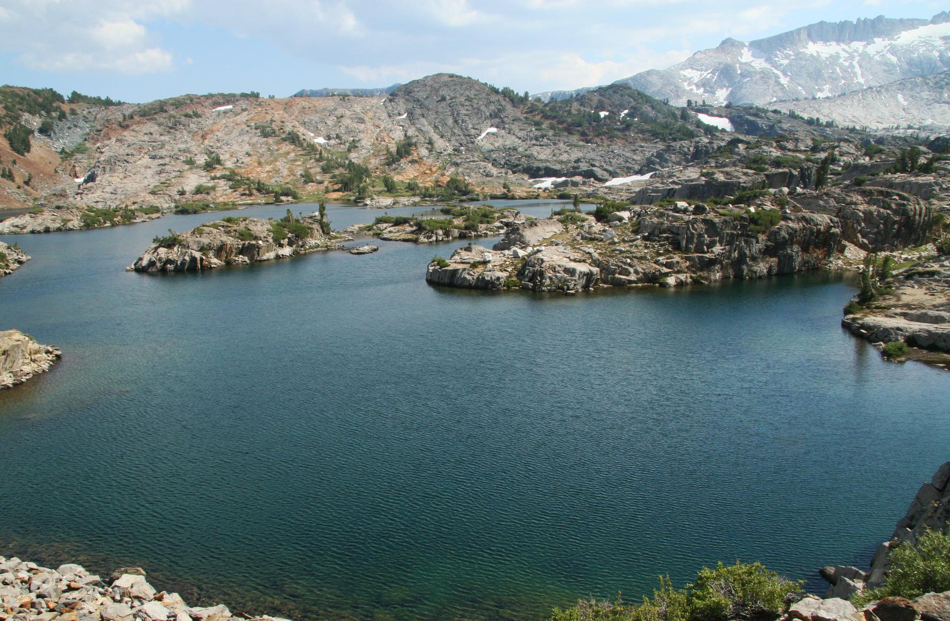 Blue-green lake with rocky islands, surrounded by barren hills and mountains.