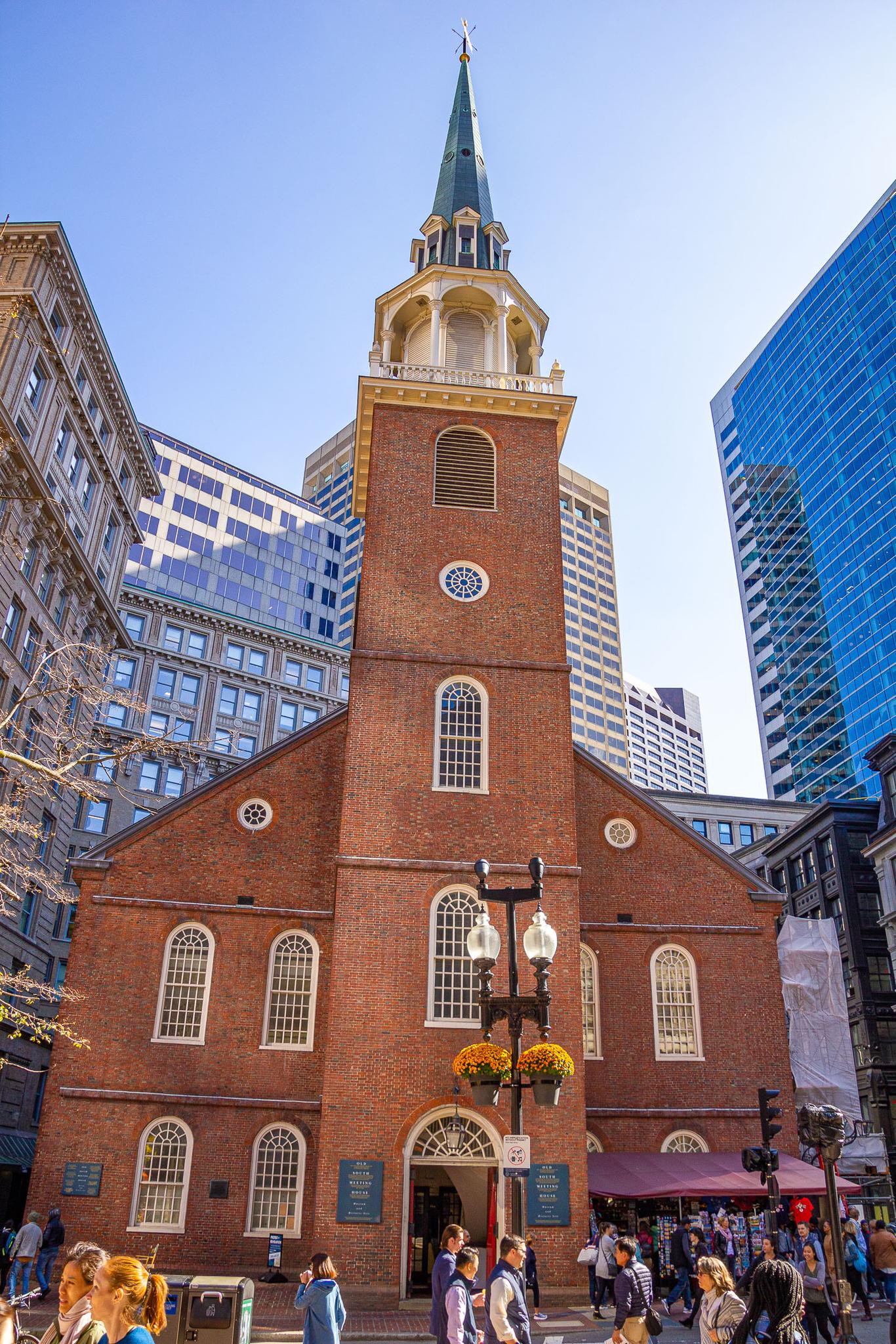 A historic brick church with a tall steeple surrounded by modern city buildings.