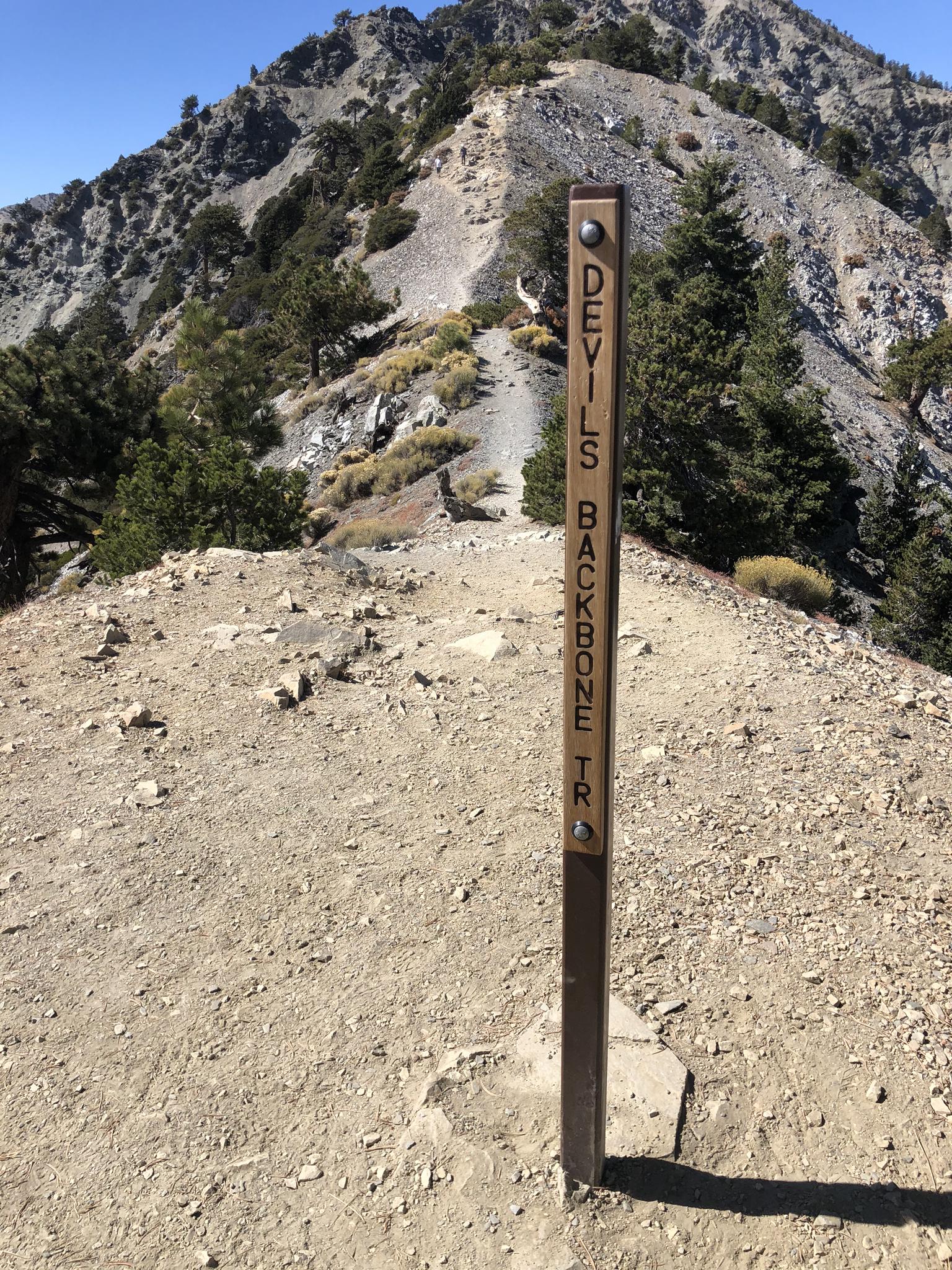 A trail marker on a rocky mountain path with steep, barren slopes beyond.