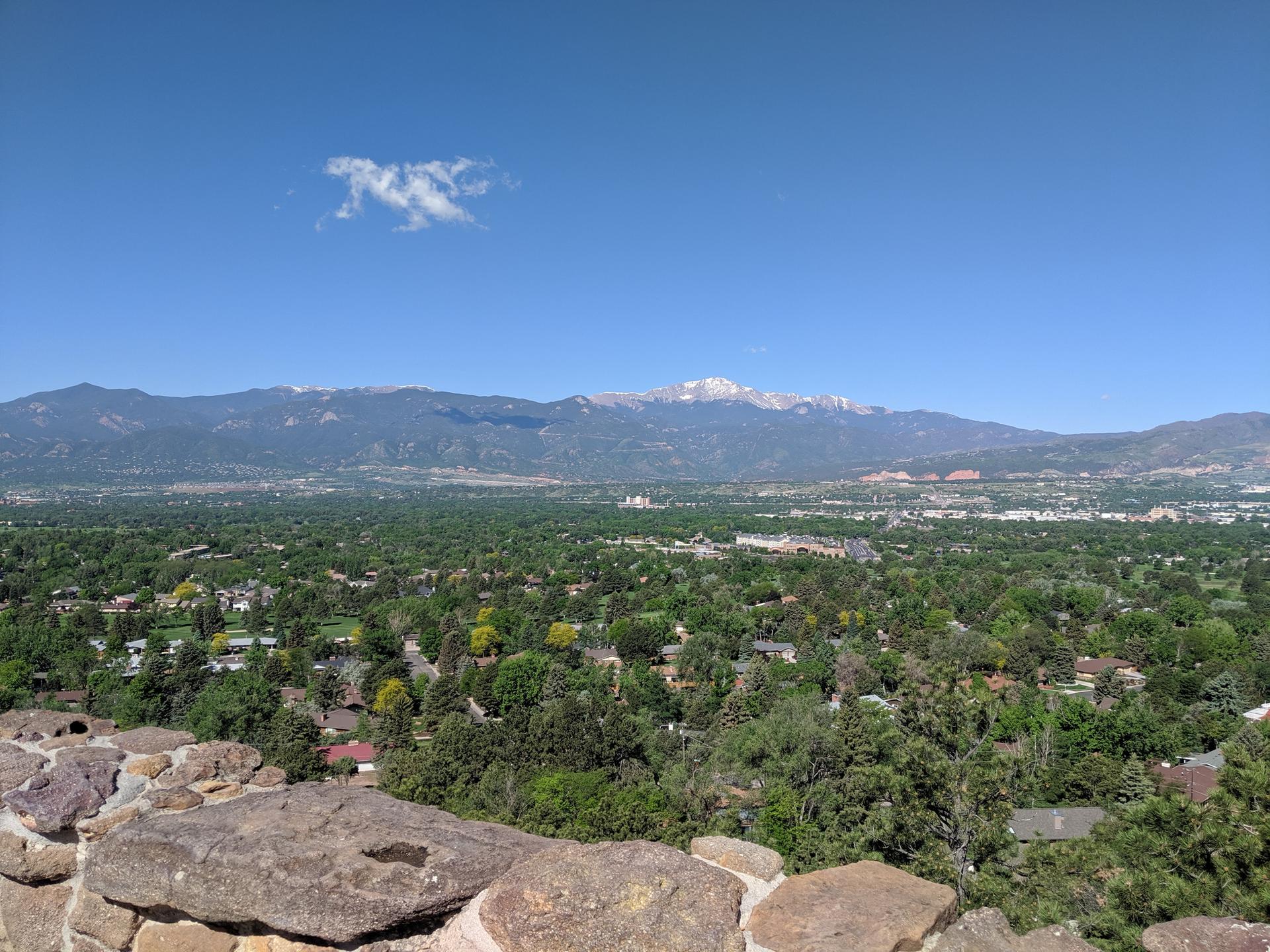 Panoramic view of a green city and snow-capped mountains under a clear blue sky.