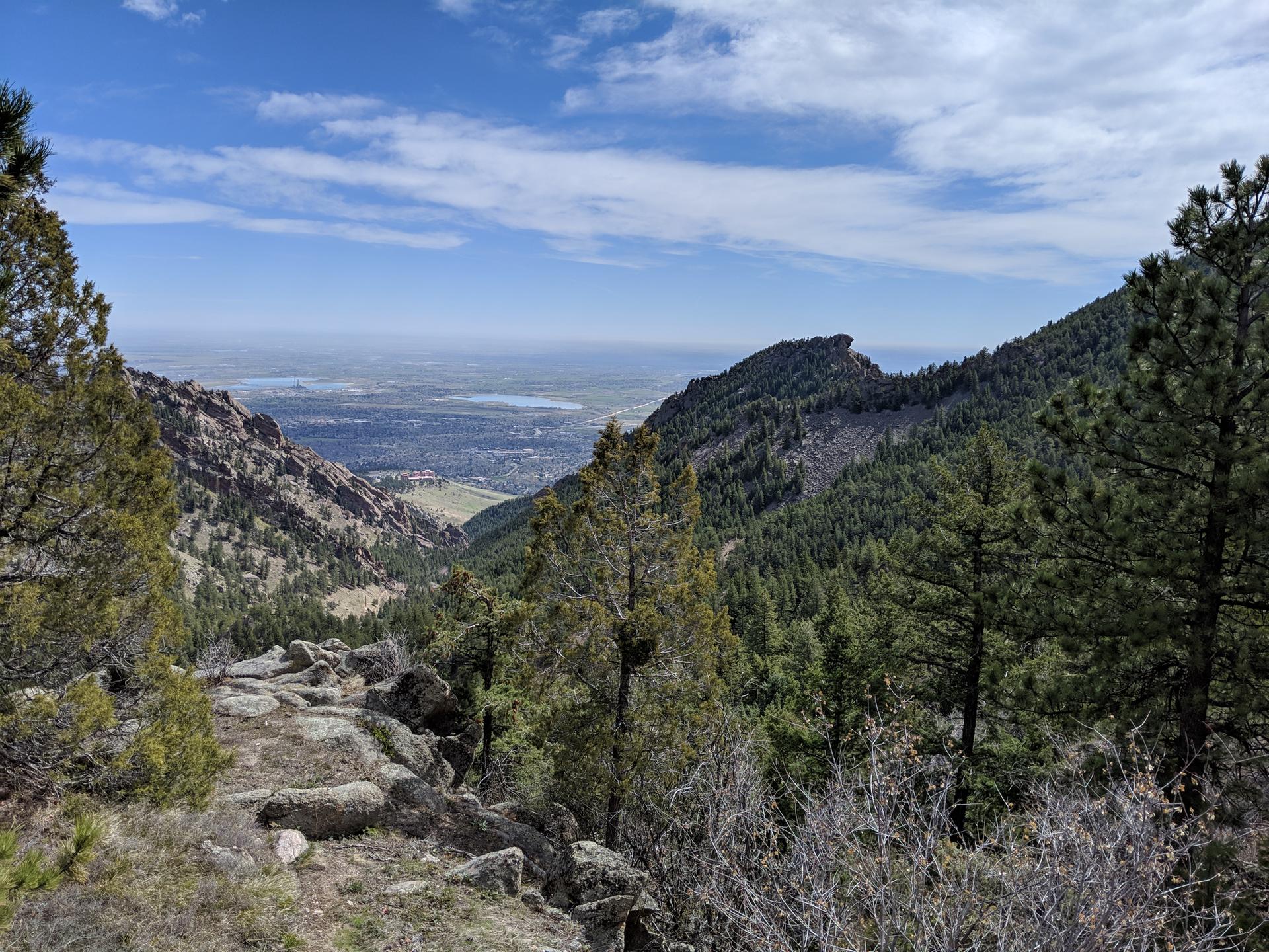 Mountain valley view with distant city, green trees, and blue sky.