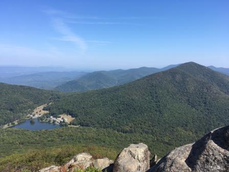 Clear day view of green mountains, a lake, and rocky foreground.