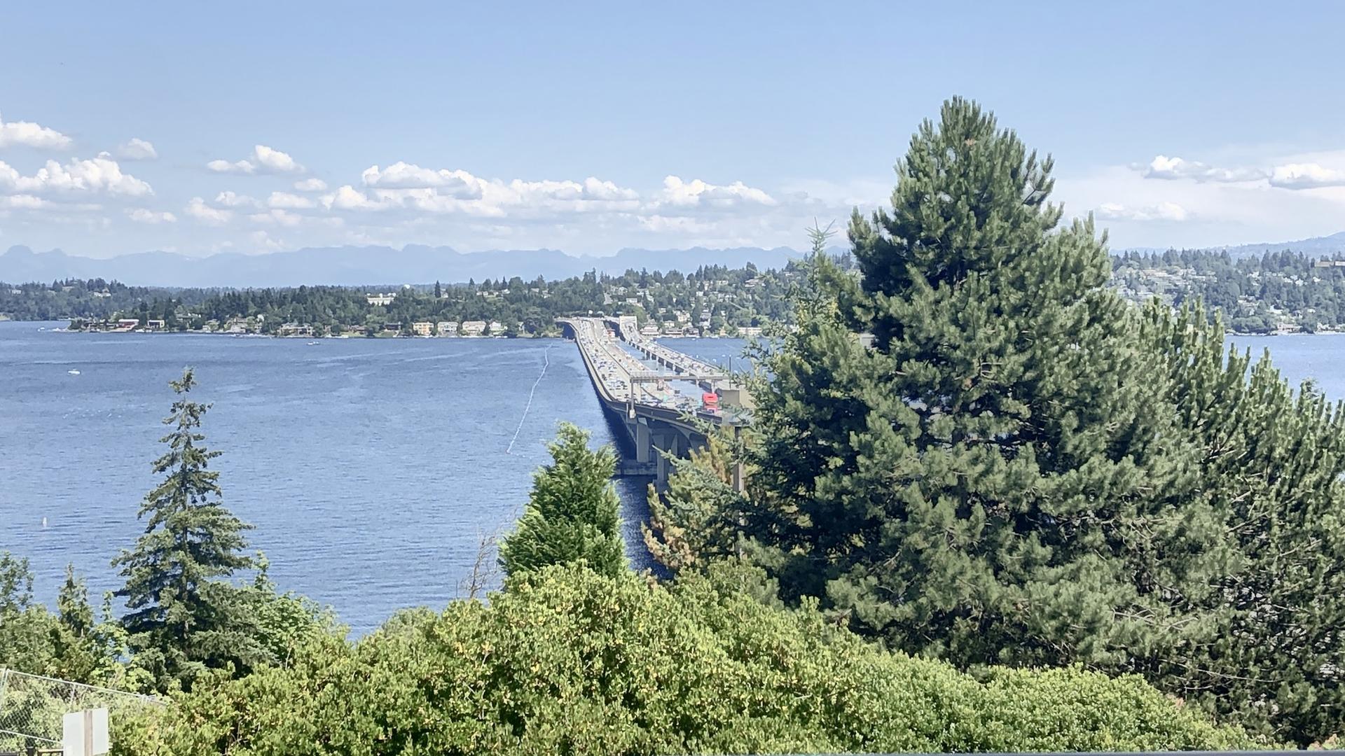 Long bridge spans blue water under a bright, cloudy sky.