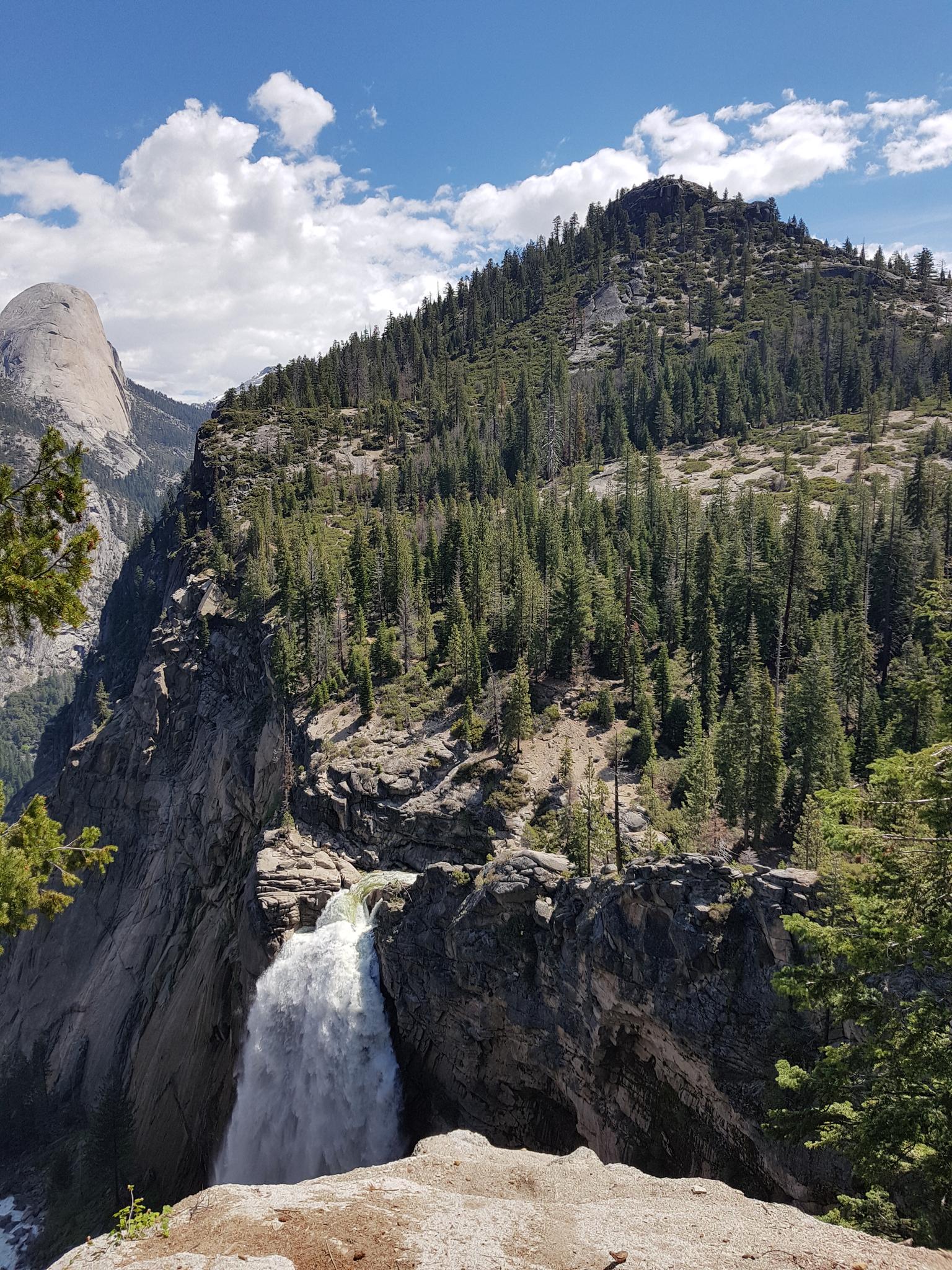 A powerful waterfall plunges from a rocky cliff face under a blue sky.