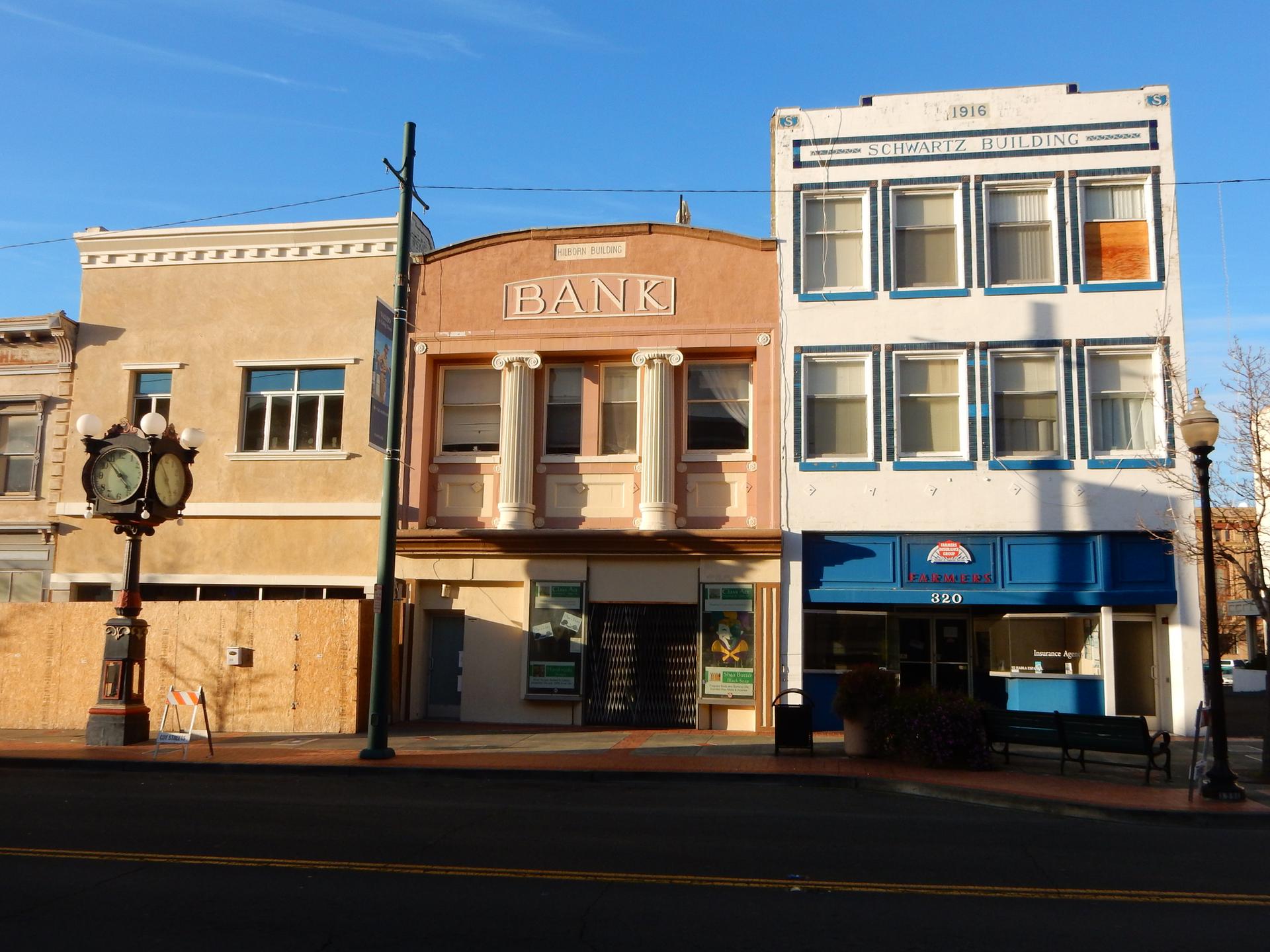 Three old buildings on a street, one labeled 'BANK', under clear sky.