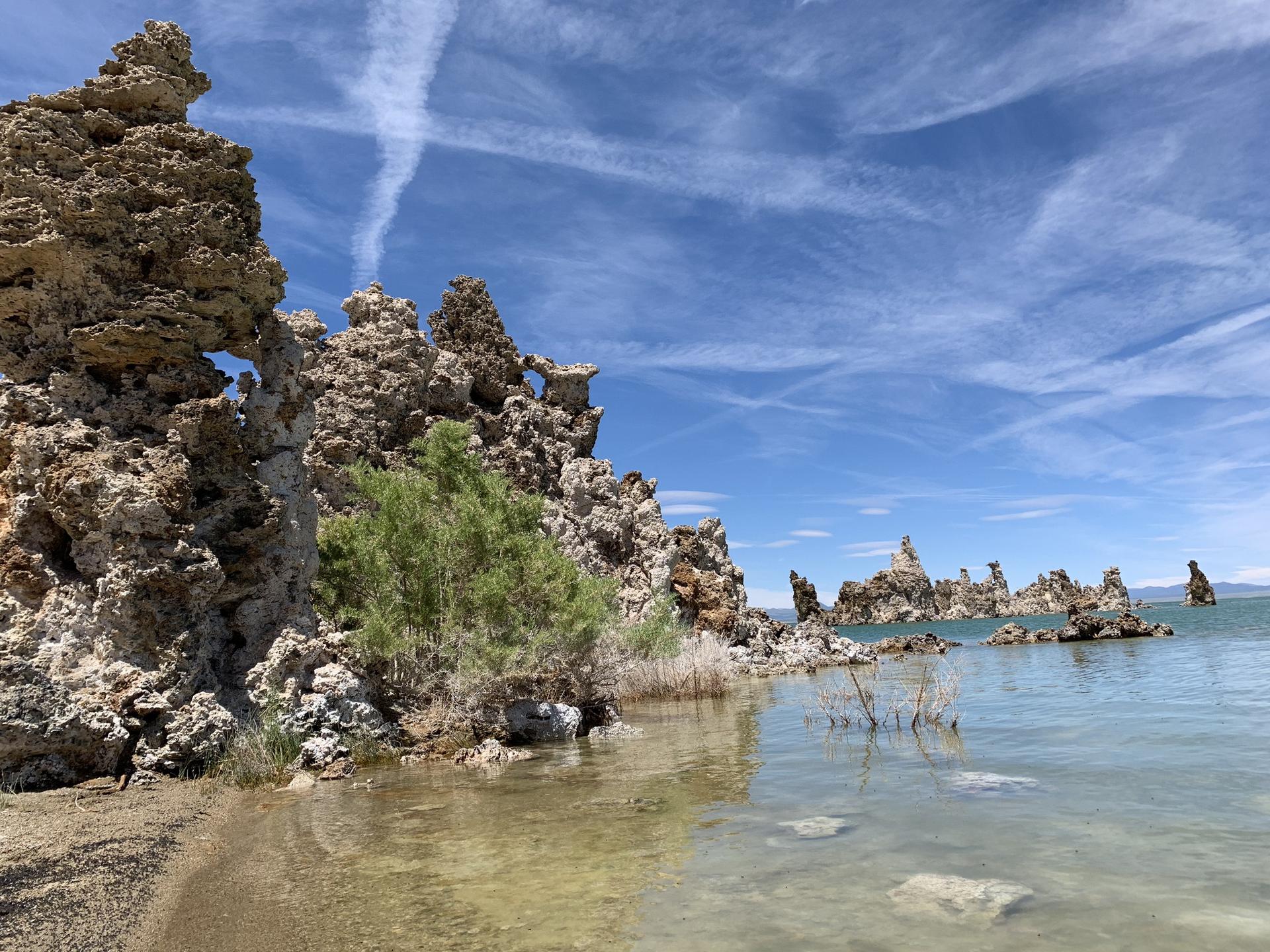 Large tufa formations on a lake shore with green bushes under a blue sky.
