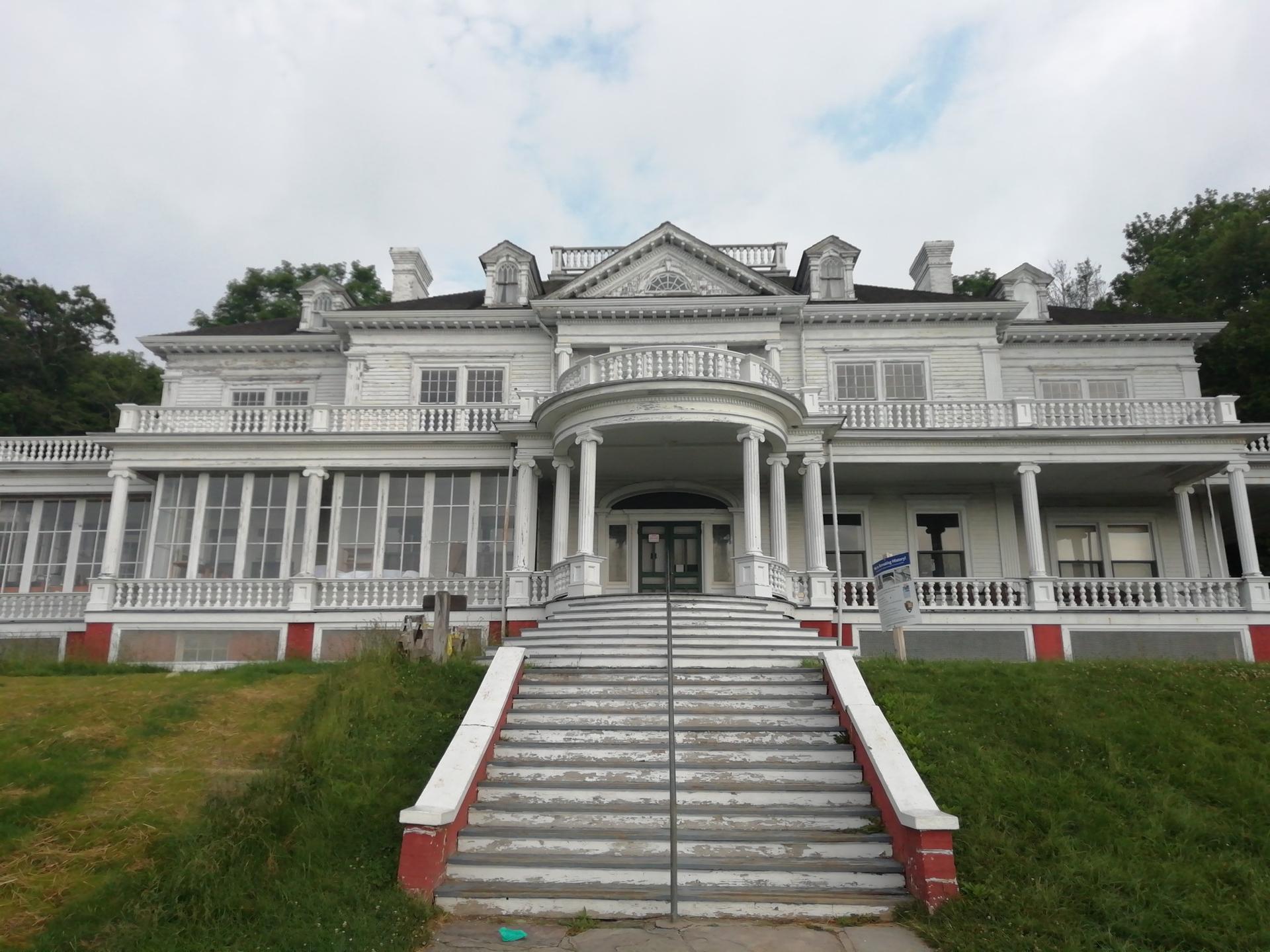 A grand white mansion with a large staircase under an overcast sky.