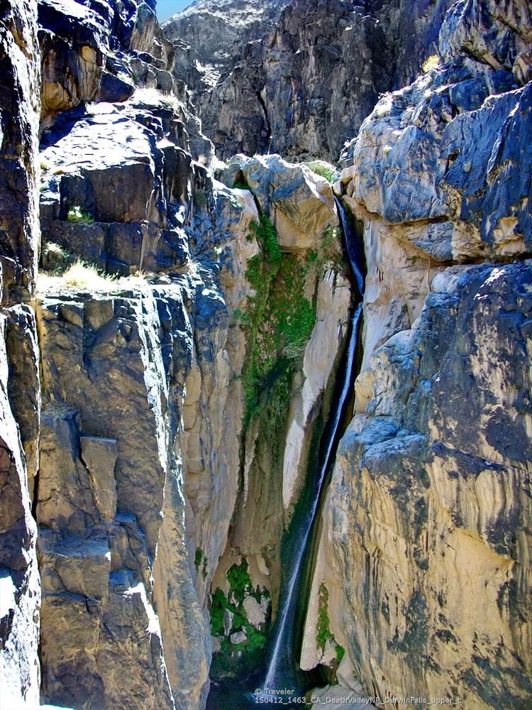 A tall, narrow waterfall plunges down a deep, sunlit rocky canyon.