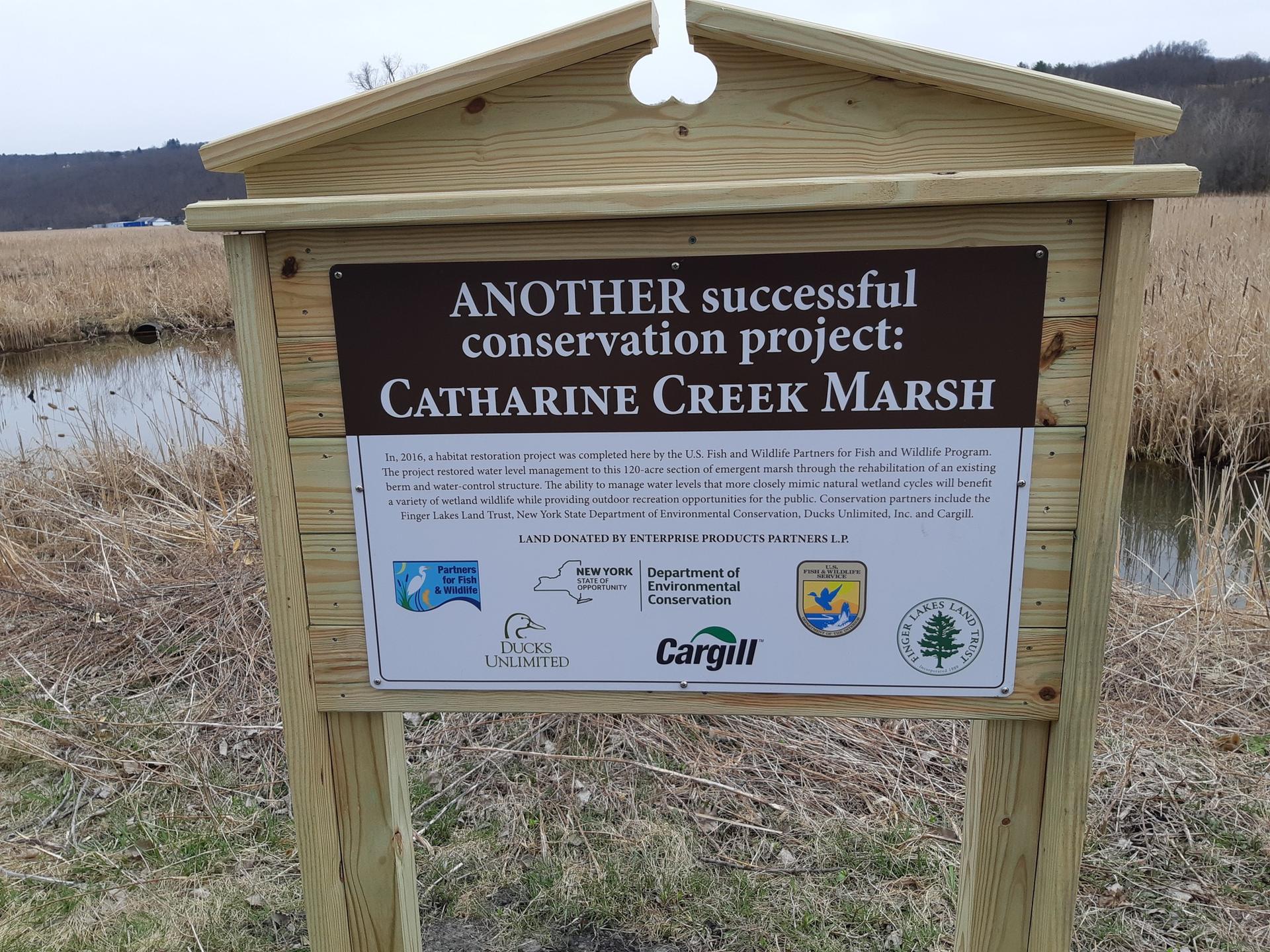 Wooden sign detailing a conservation project in a marshy landscape.