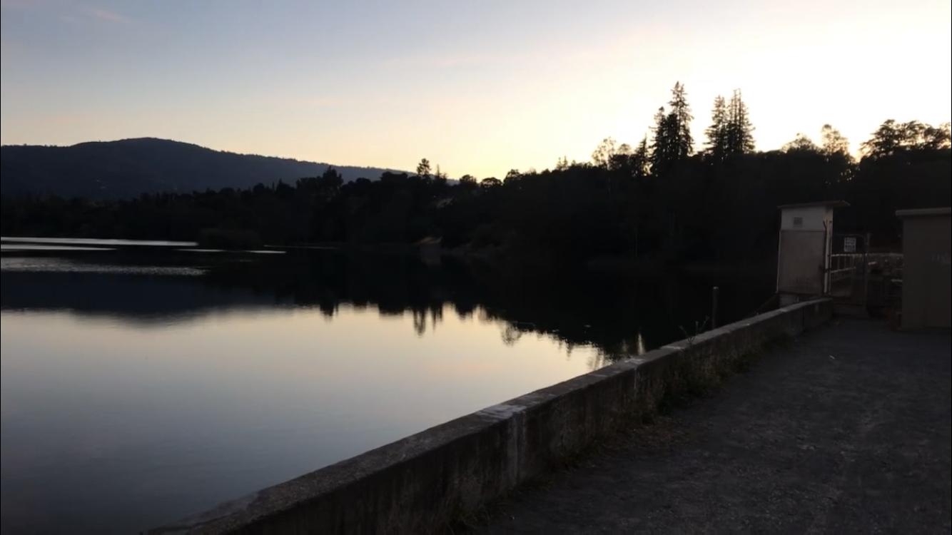 Serene lake at dusk, mountains and trees silhouetted against the sky.