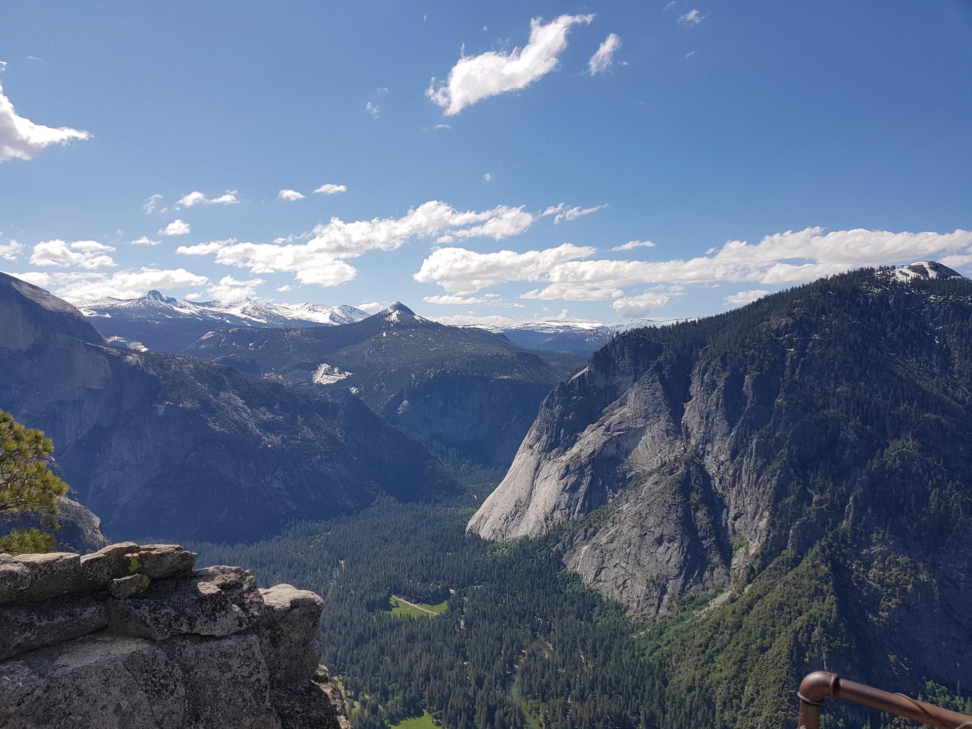 Expansive mountain valley with forests, rocky cliffs, and distant snow-capped peaks.