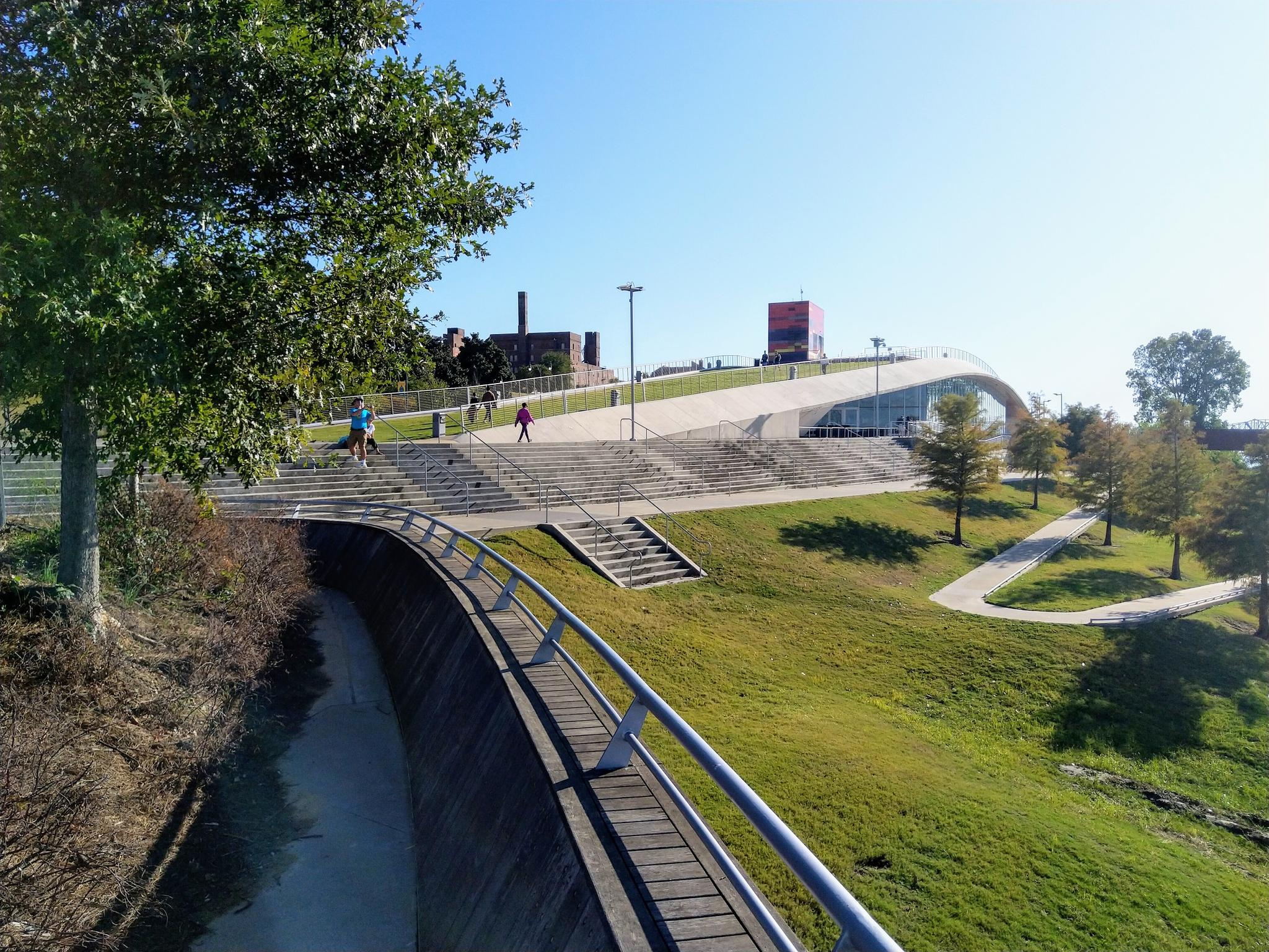 Modern park with curved walkways, green hills, and people walking.