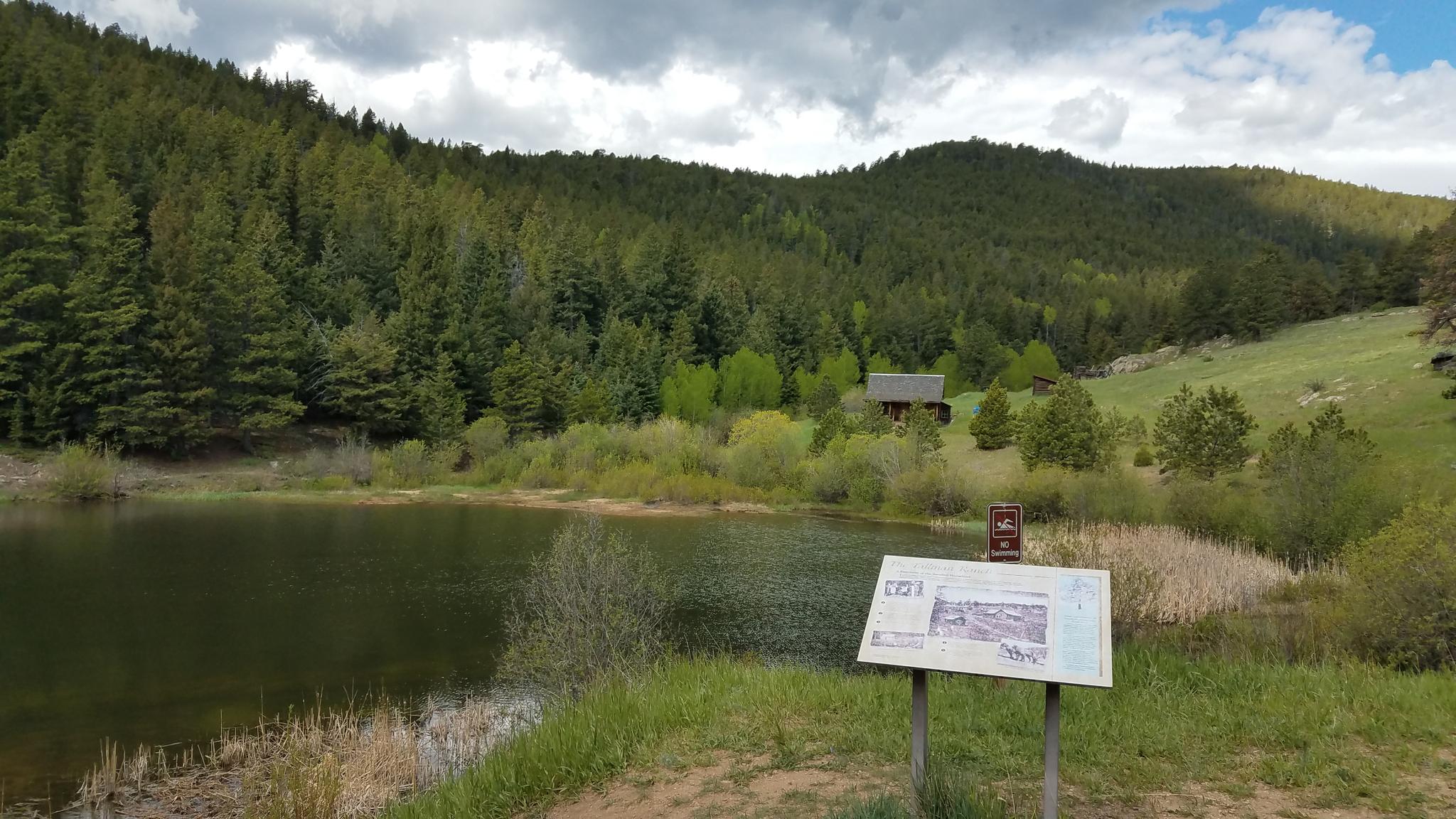 A lake with forested mountains, a distant cabin, and an information sign.