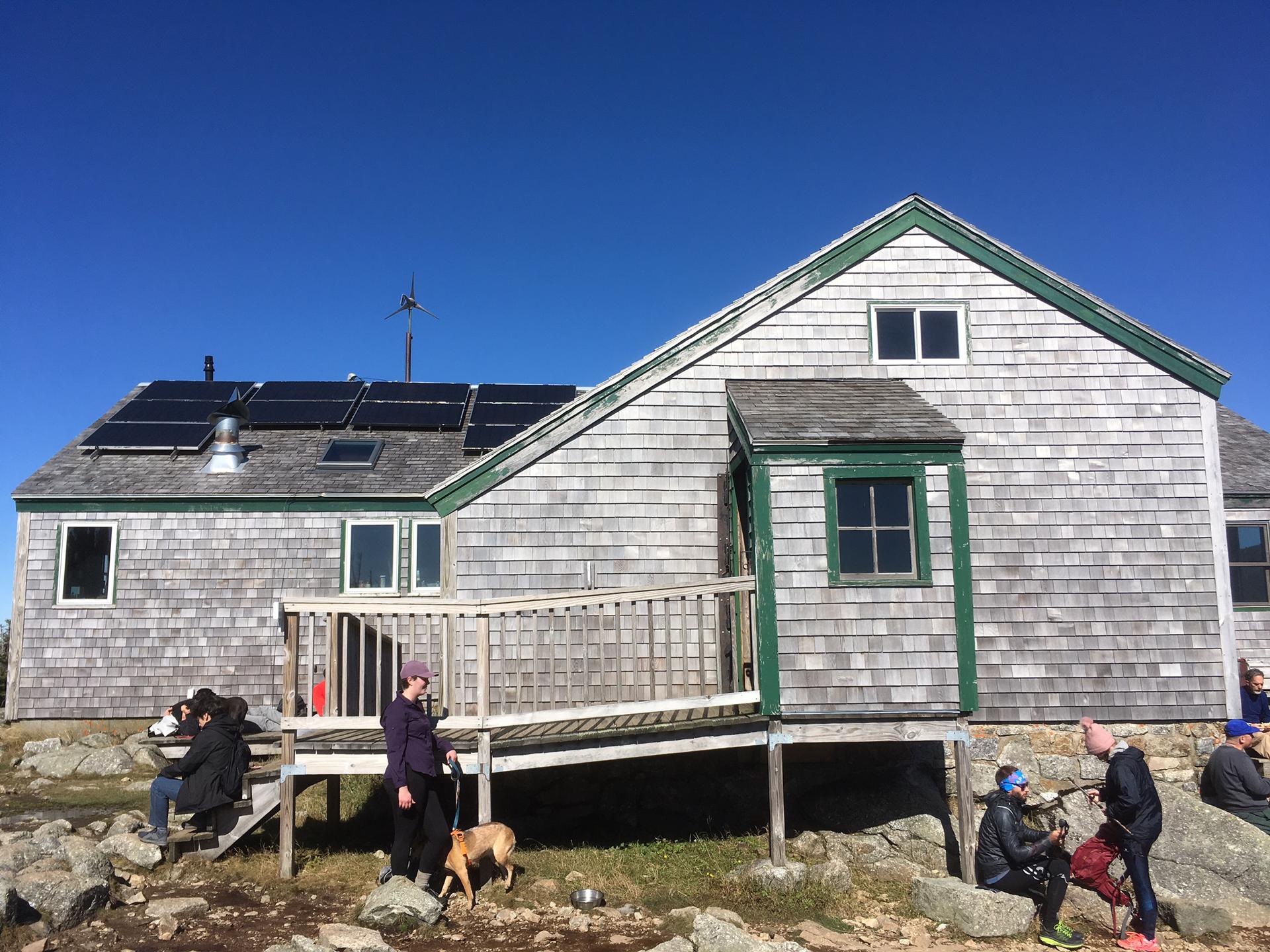 Shingled building with solar panels, people and a dog outside on a sunny day.
