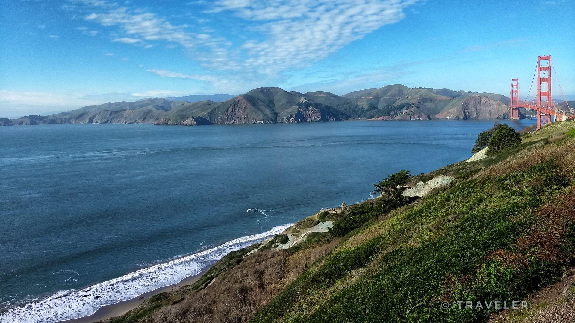 Panoramic view of a large bay, distant mountains, and a red bridge.
