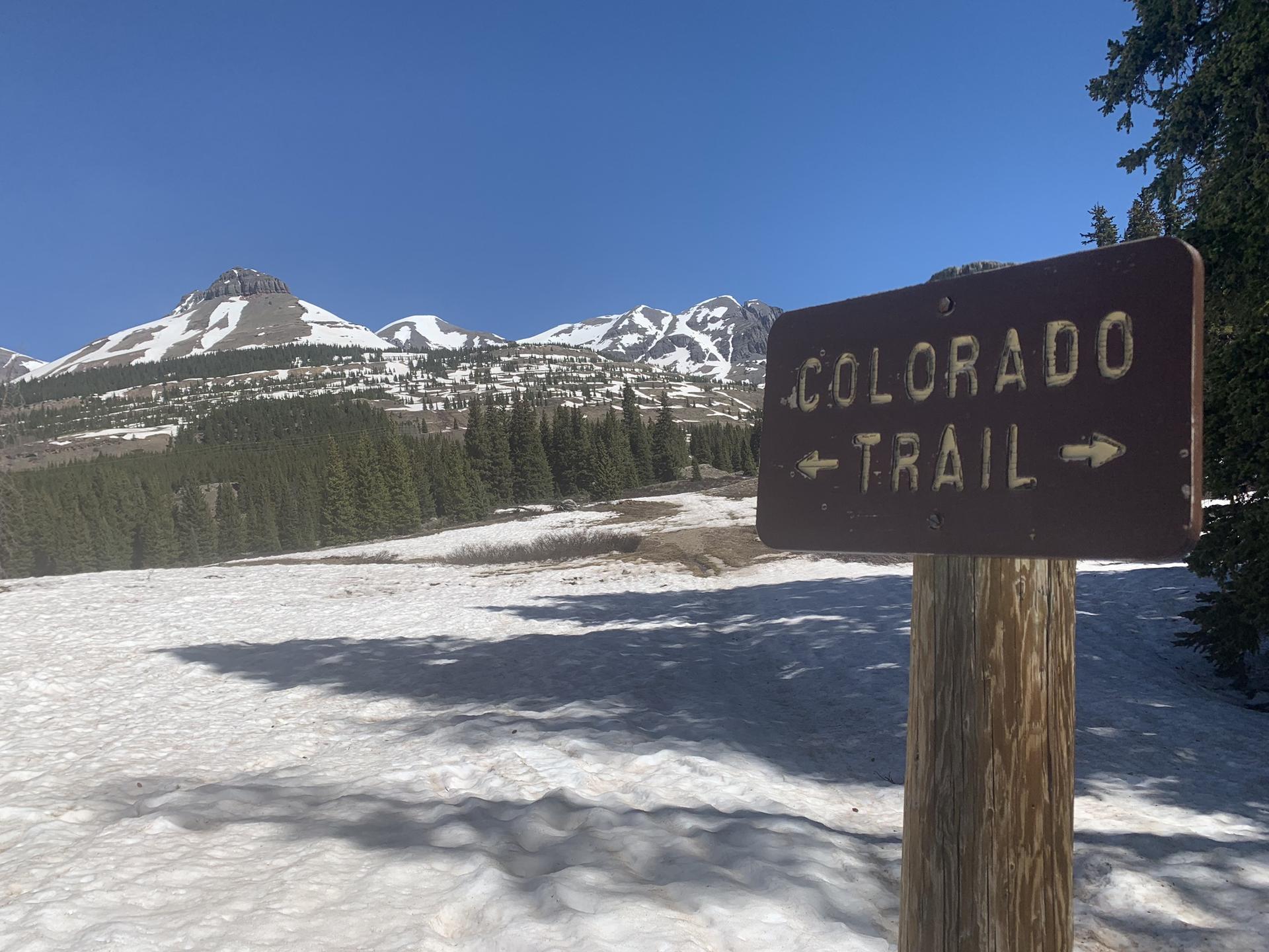 A brown trail sign stands in deep snow on a bright sunny day.